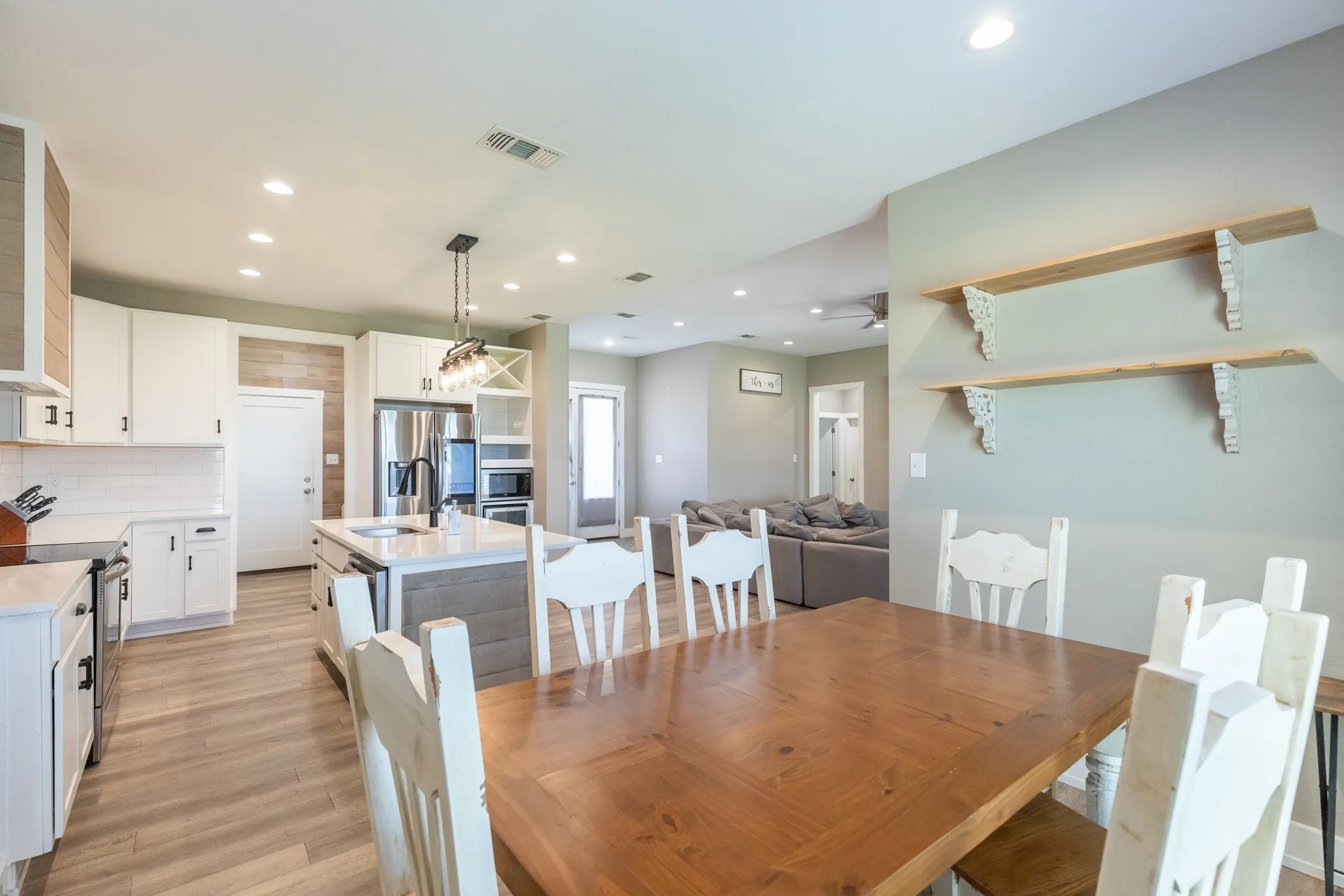 Open-concept kitchen and dining area featuring light-toned wood-finish flooring, white cabinetry, a kitchen island with sink, and stainless steel appliances