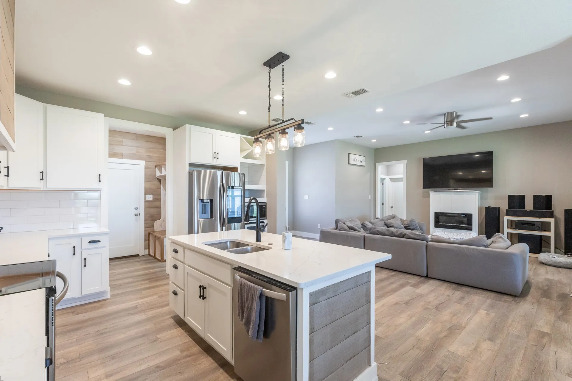 Modern kitchen featuring white cabinetry, a central island with a double basin sink, stainless steel appliances, and a subway tile backsplash