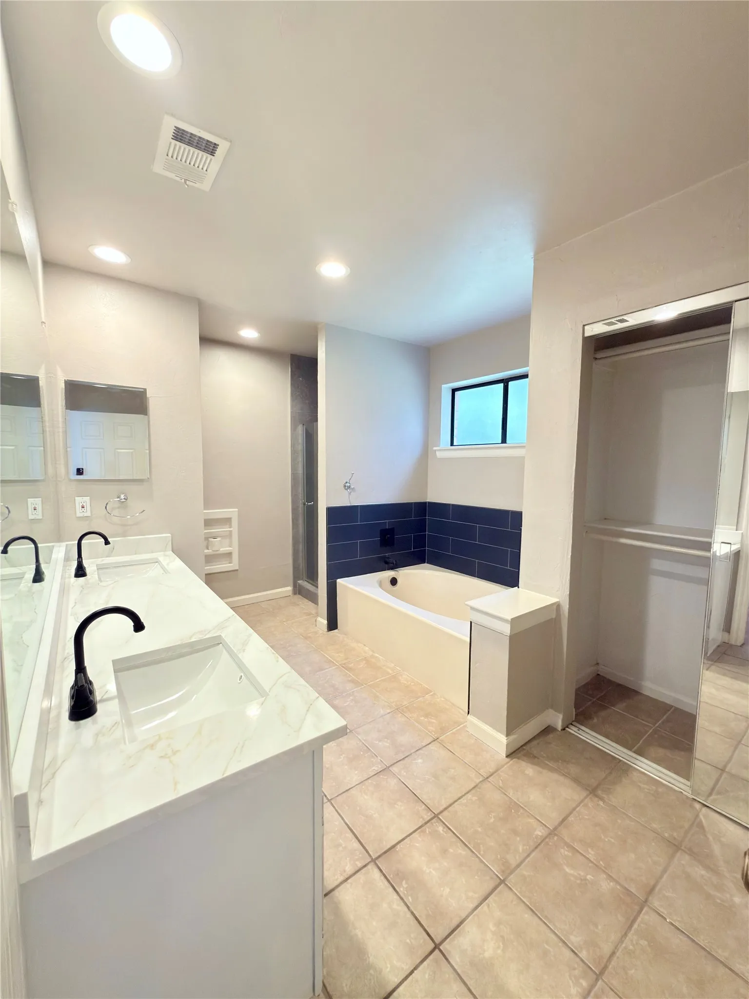 Bathroom featuring a dual vanity with white cabinetry, marbling countertops, and matte black fixtures