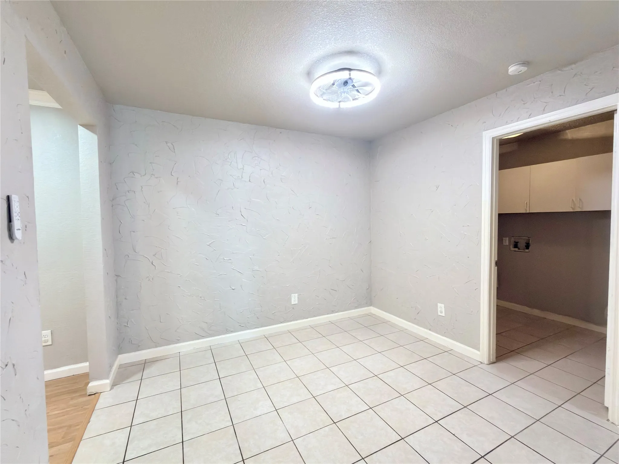Room featuring light-colored tile flooring, textured walls, and a flush-mount ceiling light