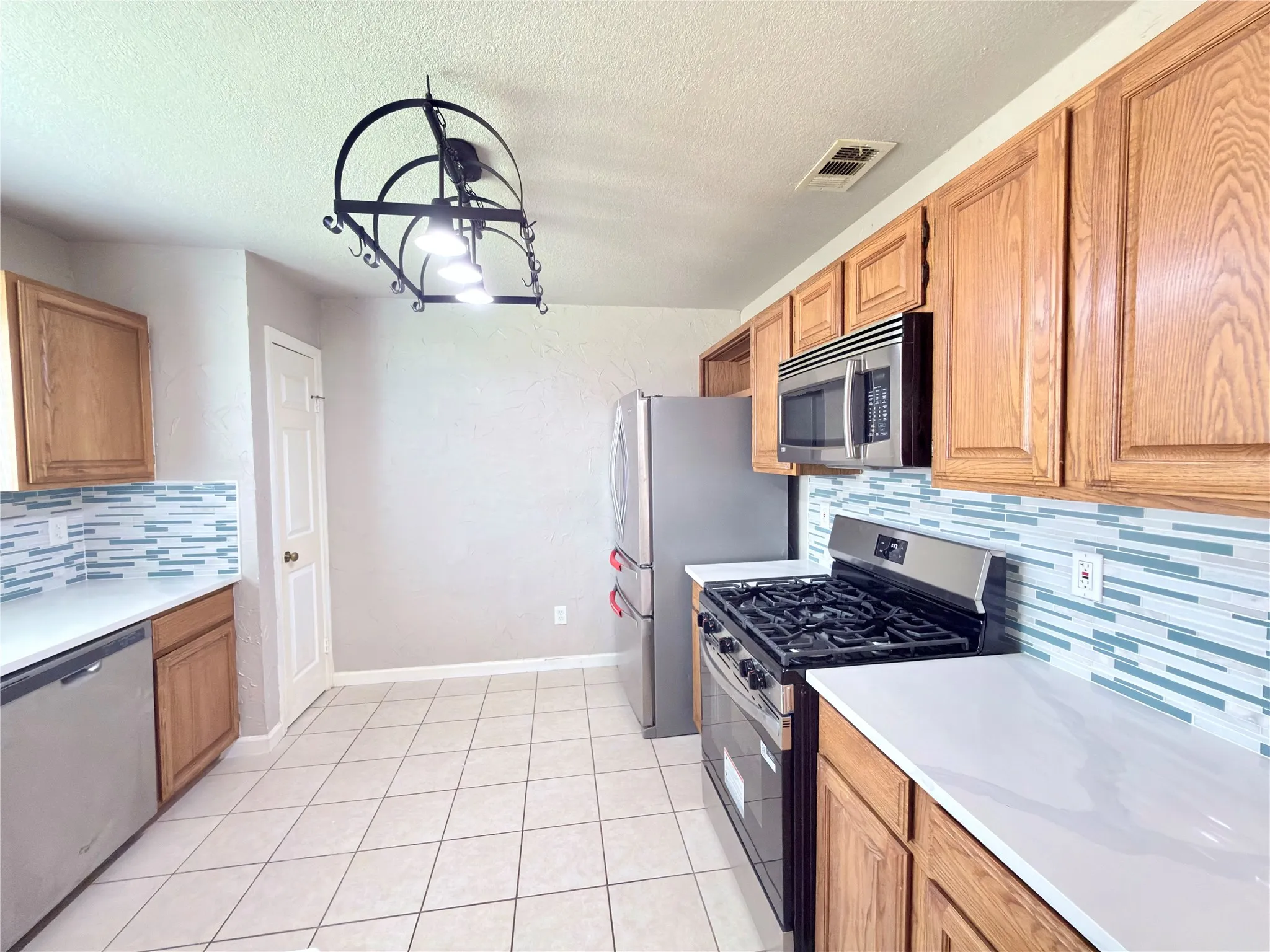 Kitchen featuring ceramic tile flooring, wood cabinetry, stainless steel appliances, white countertops, and a decorative tile backsplash