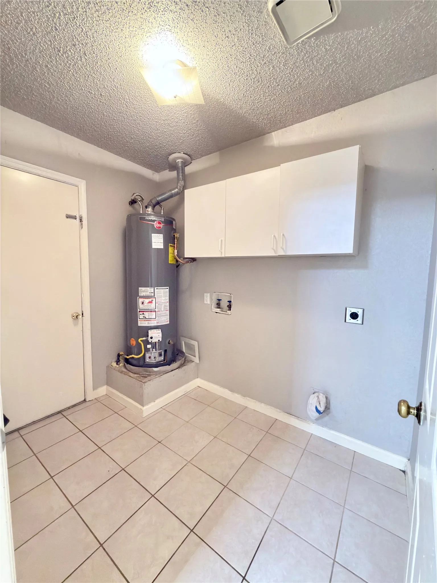 Laundry area featuring neutral tile flooring, built-in overhead cabinetry, and a water heater on a raised platform