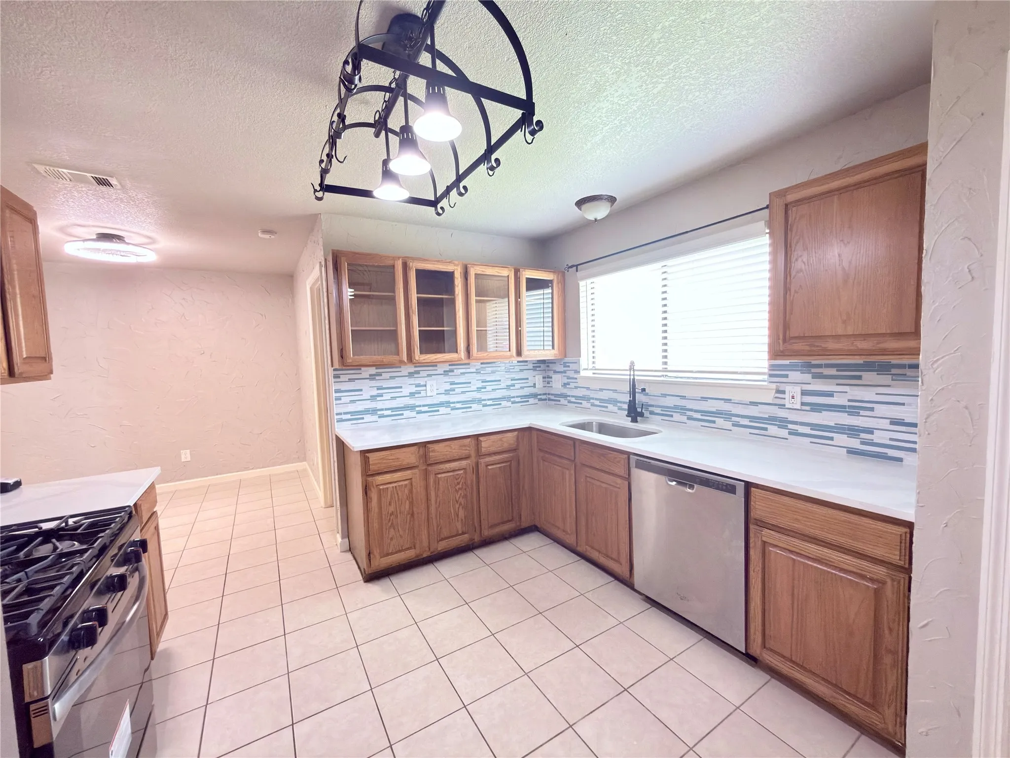 Kitchen featuring wood cabinetry, white countertops, stainless steel appliances, a tile backsplash, and tile flooring