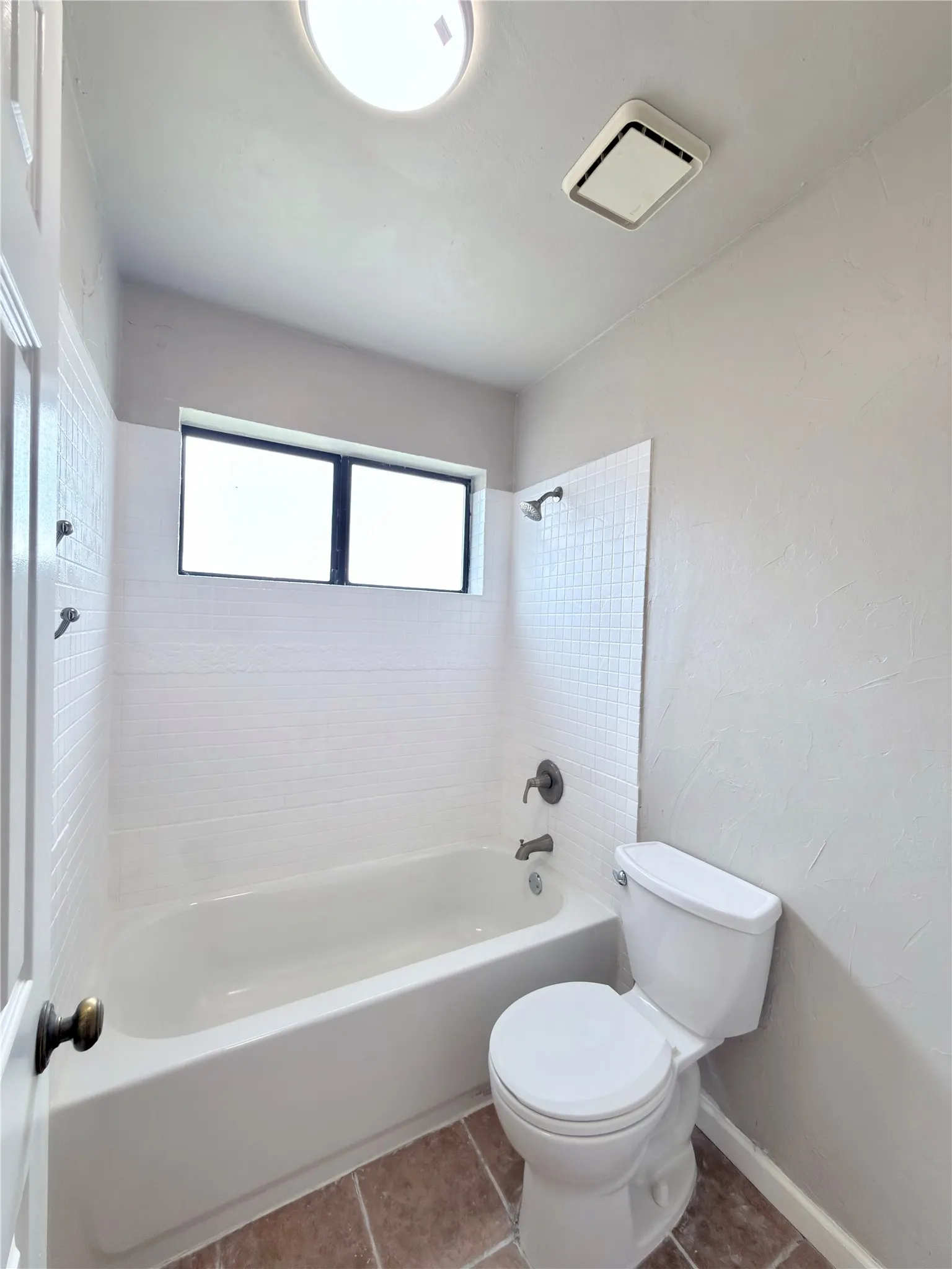 Bathroom featuring a white bathtub with subway tile surround, a toilet, and a window