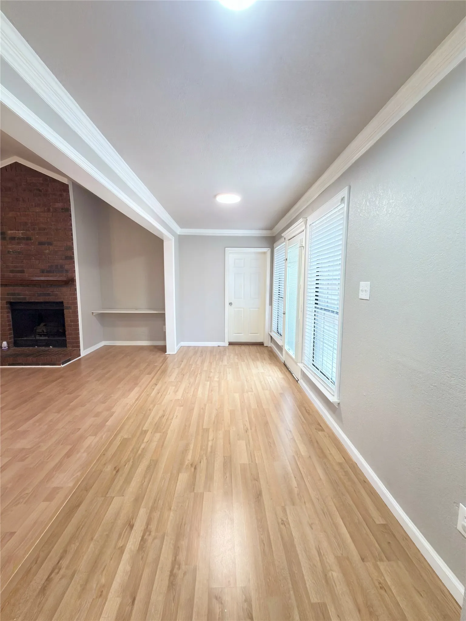 Expansive room featuring wood-finish flooring, a red brick fireplace, and multiple windows with blinds