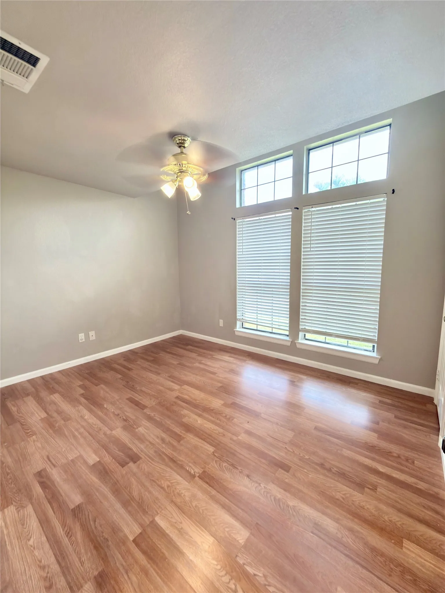Spacious room featuring wood-finish flooring, neutral wall tones, and a ceiling fan with integrated lighting