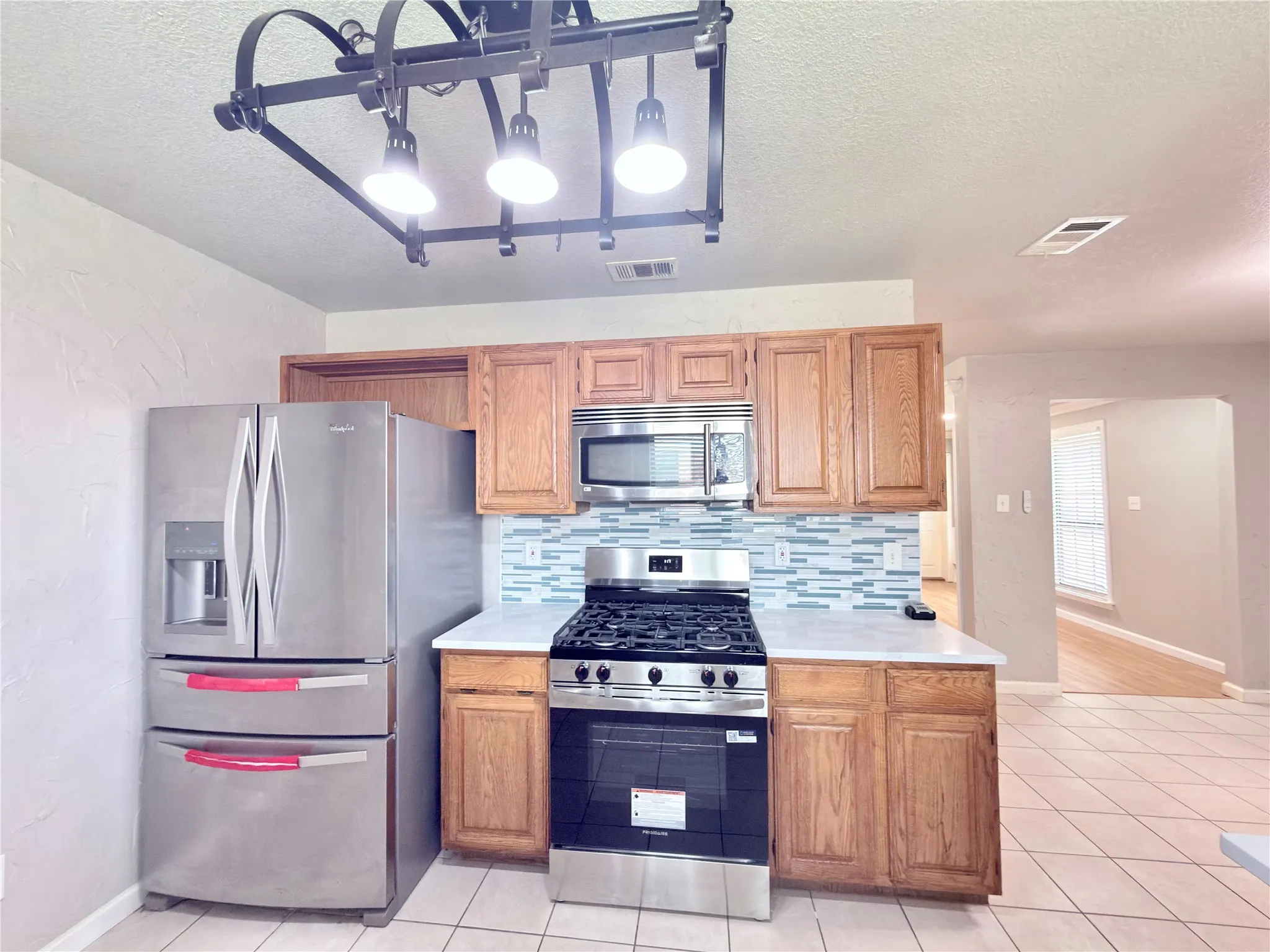 Kitchen featuring stainless steel appliances, wood cabinetry, a tiled backsplash, and tile flooring