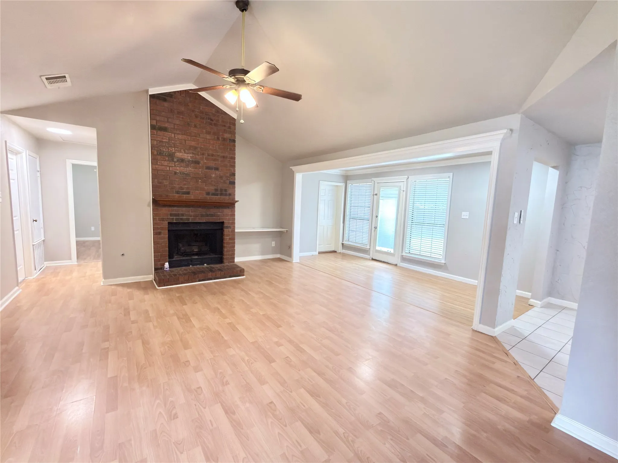 Living area featuring a brick fireplace, vaulted ceiling with a ceiling fan, wood-finish flooring, and double glass-paneled doors with side windows
