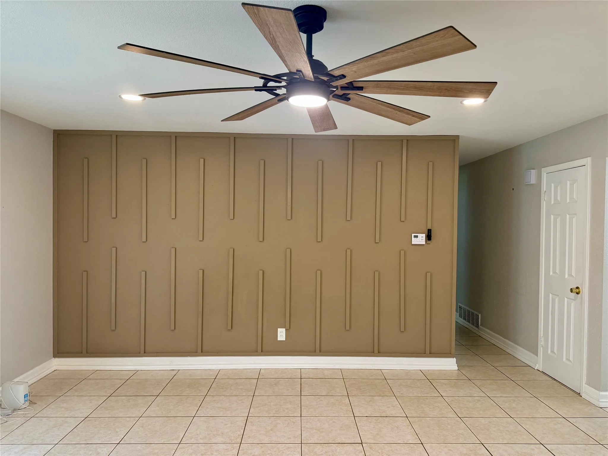 Accent wall with vertical paneling, contemporary ceiling fan with integrated lighting, recessed ceiling lights, tiled flooring, and a paneled interior door