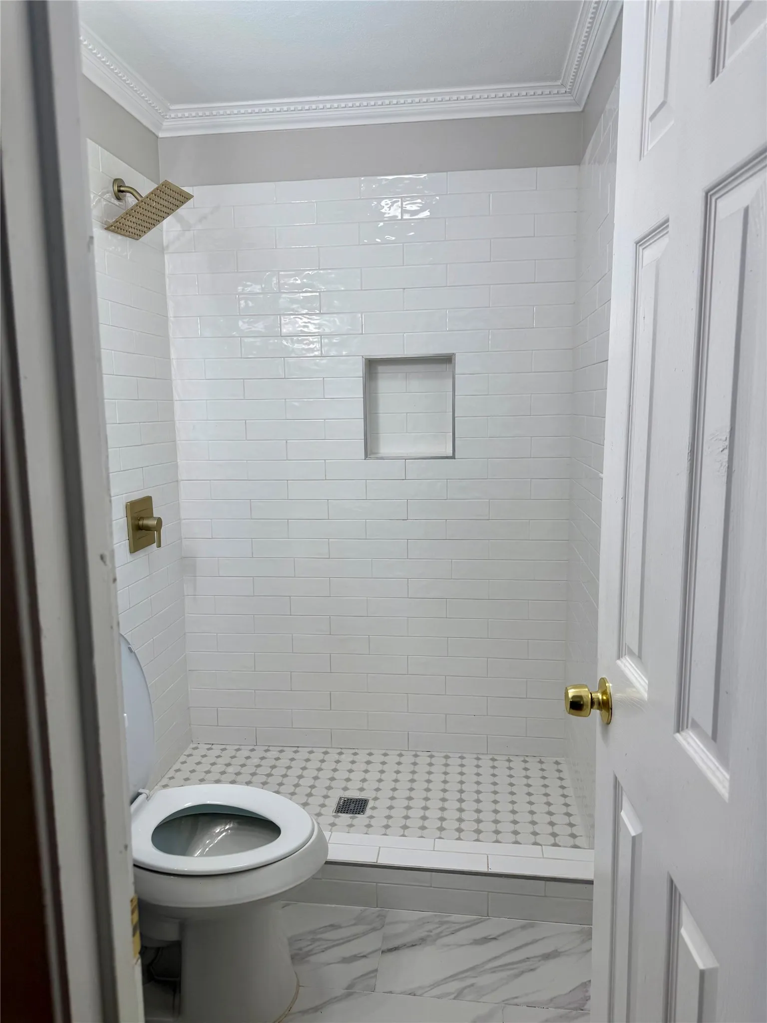 Modern shower with white subway tile, a brass rain showerhead, a recessed niche, and a patterned shower pan