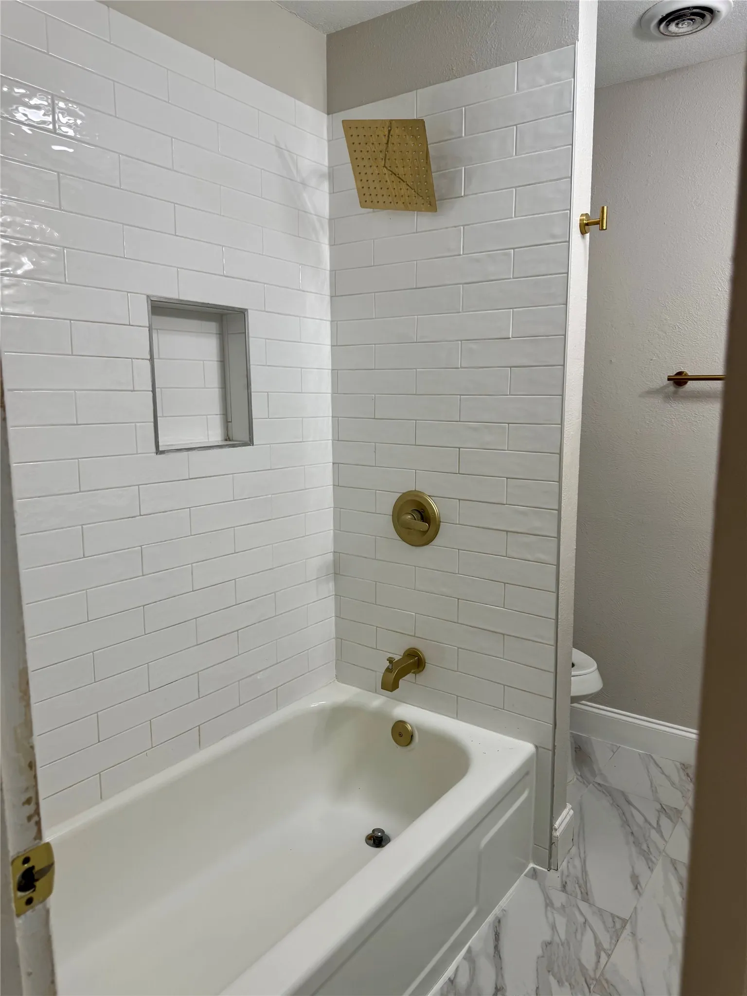 Bathtub with white subway tile surround, gold-finish fixtures, and a rain shower head