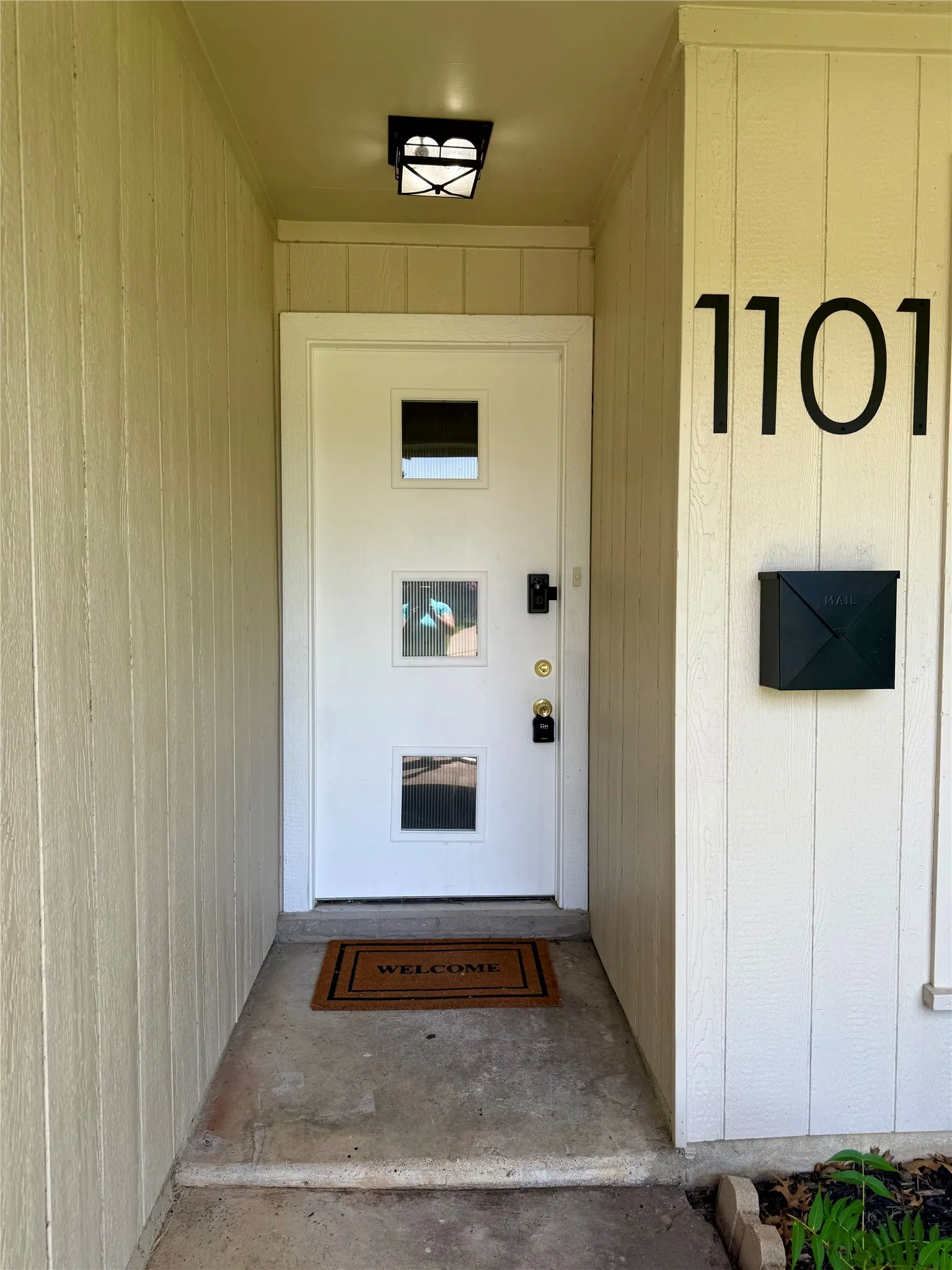 Front entry featuring a white door with multiple square lites, black house numbers, a black wall-mounted mailbox, and a flush-mount overhead light fixture