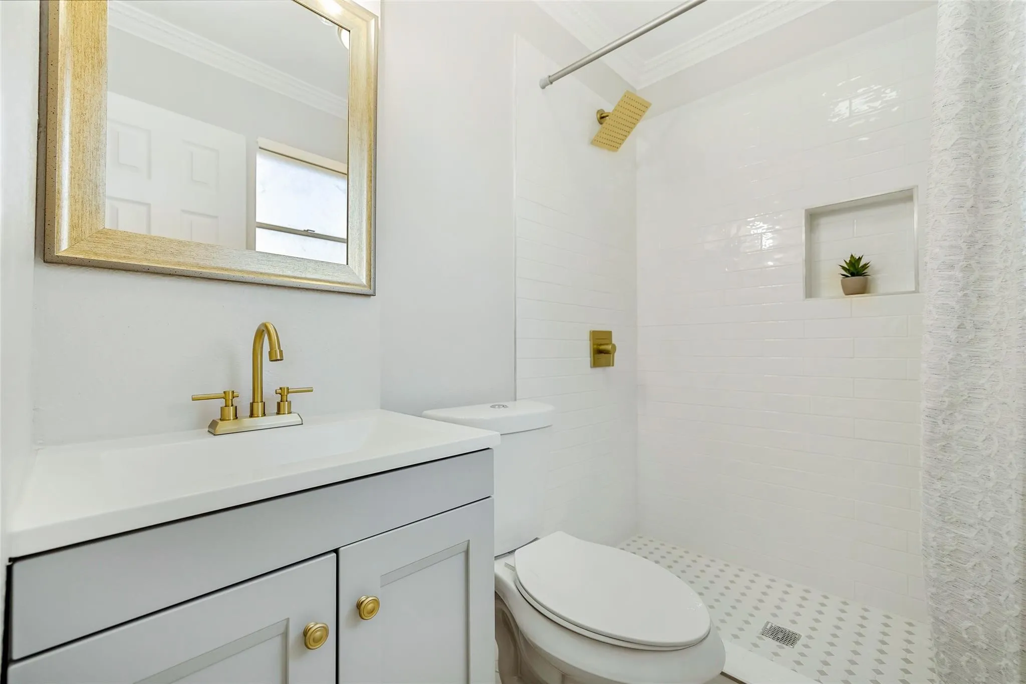 Modern bathroom featuring a white subway tile shower, gold-finish fixtures, a built-in shower niche, a light gray vanity with a white countertop, and a framed mirror