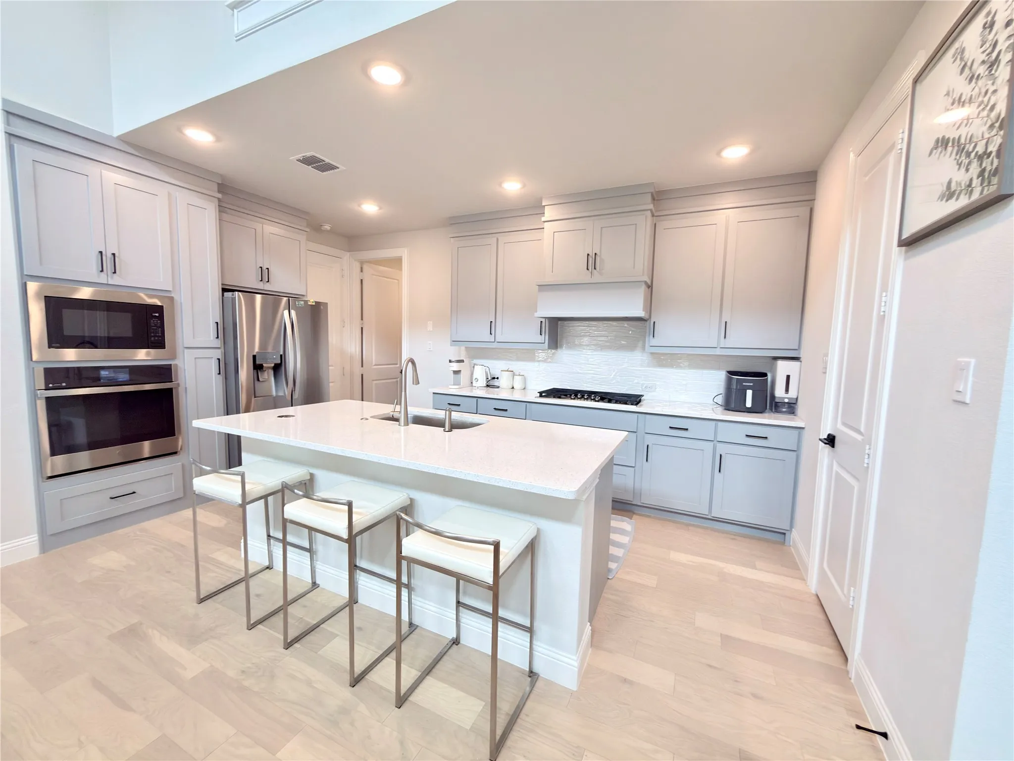 Modern kitchen featuring light gray cabinetry, stainless steel appliances, a center island with countertop seating, and light wood-finish flooring