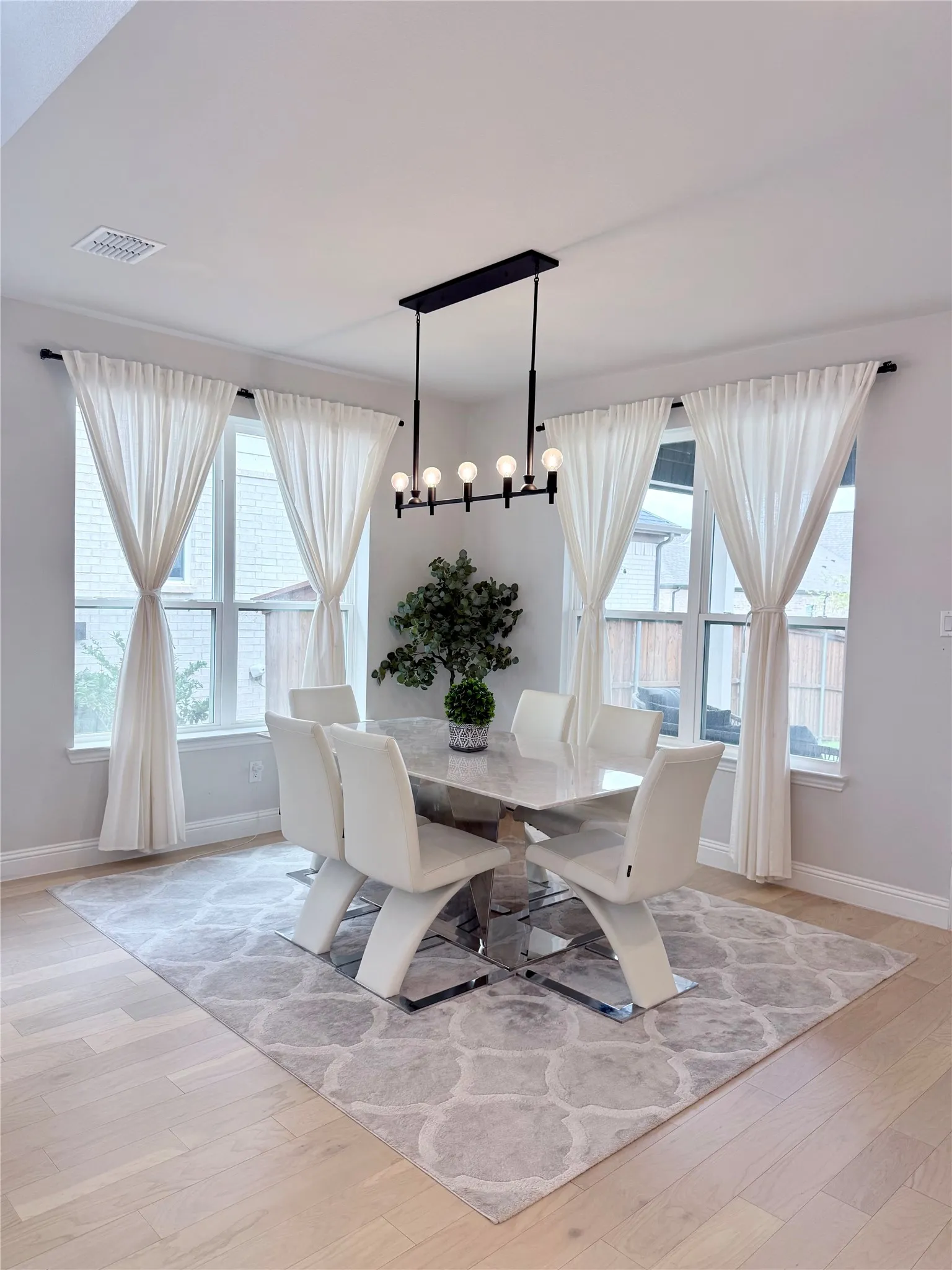 Dining area featuring a contemporary linear chandelier, multiple windows, light wood-finish flooring, and light gray wall paint