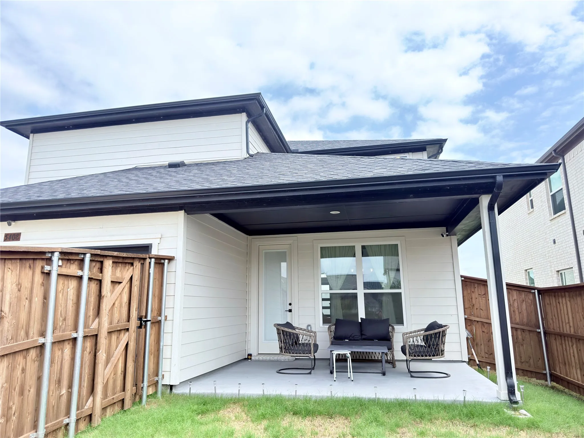 Covered patio with a concrete surface, white siding, dark gutters, and a wood fence enclosing the yard