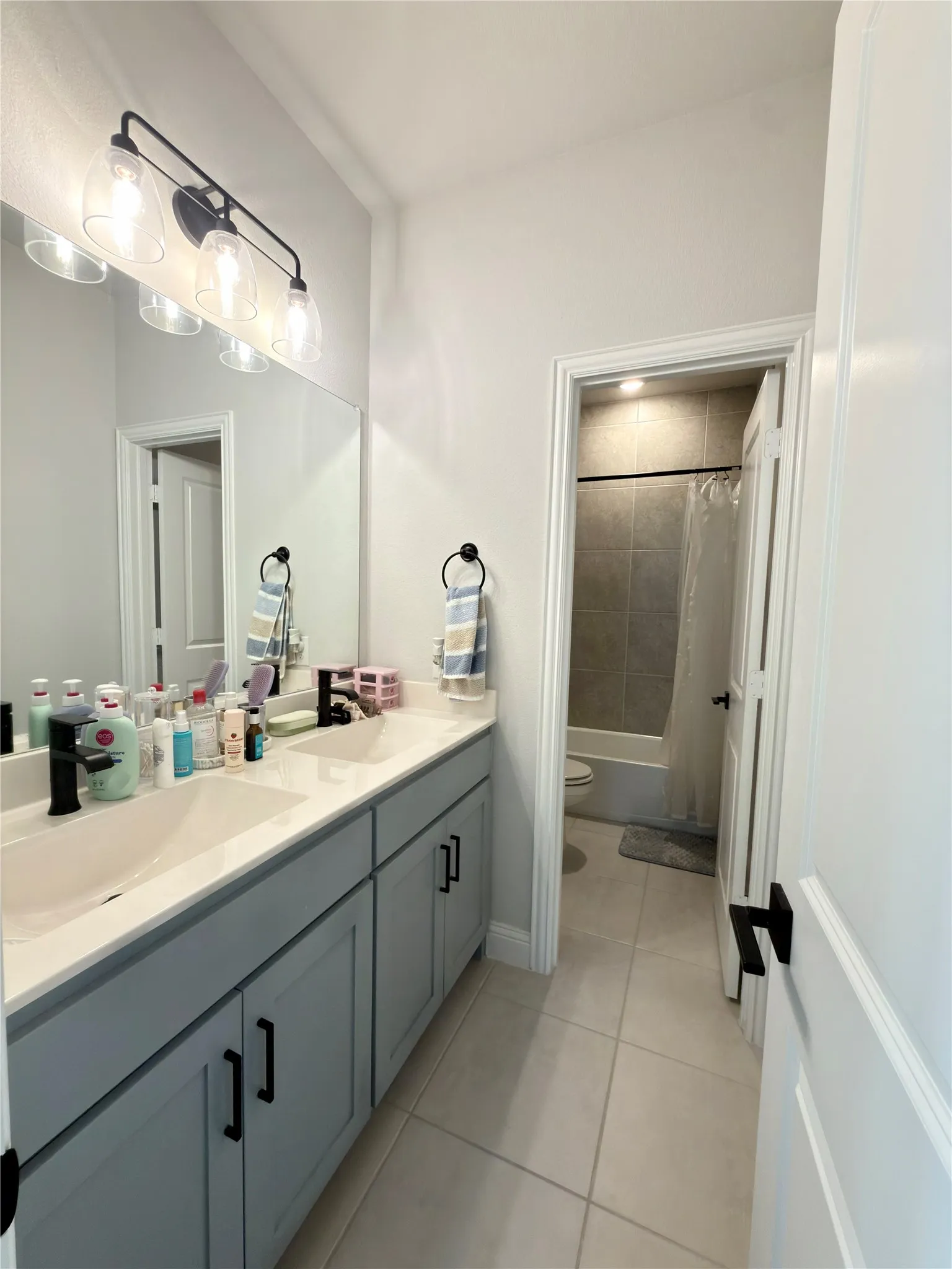 Bathroom vanity with dual undermount sinks, light gray cabinetry, and matte black hardware