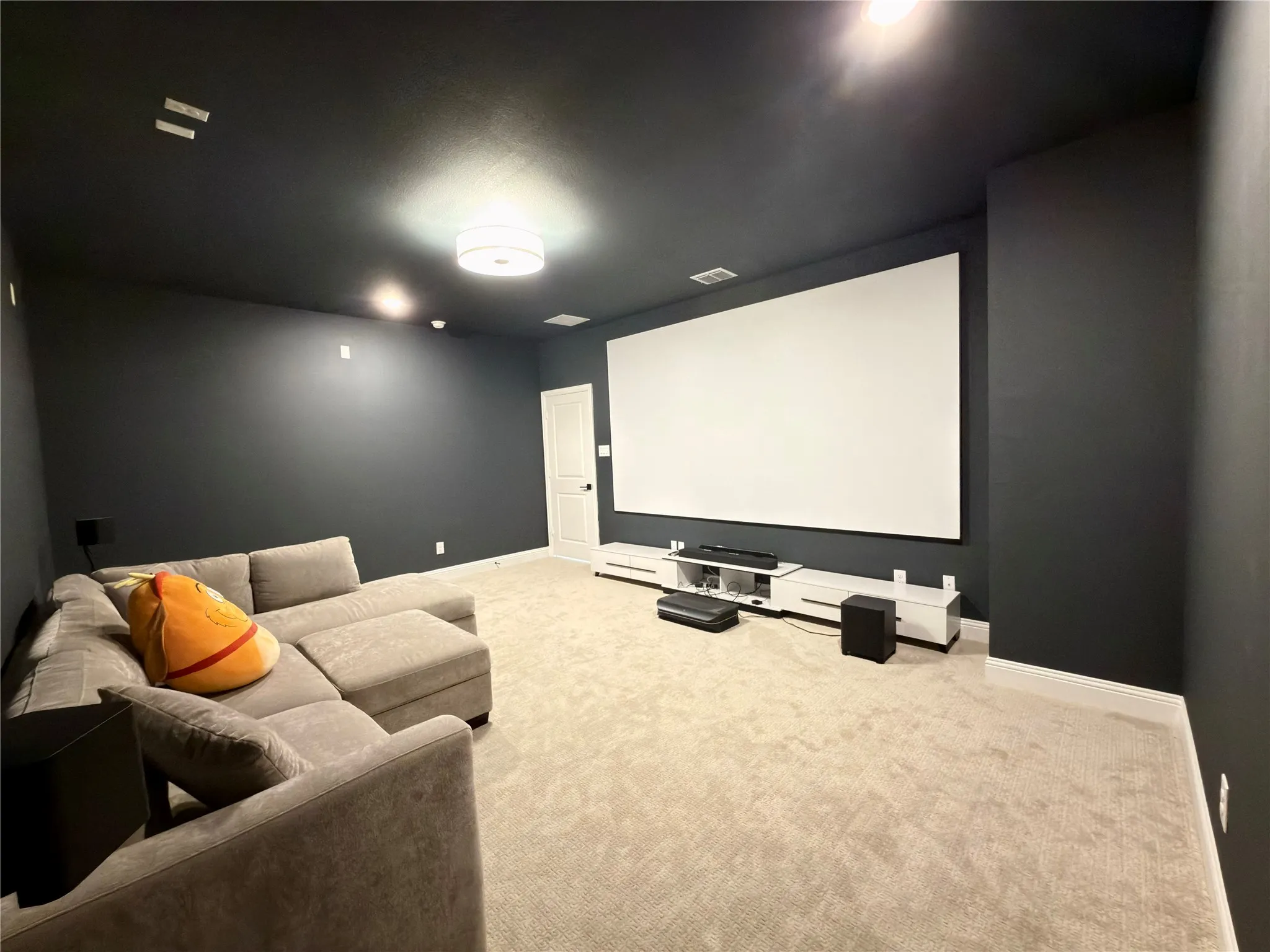 Dedicated media room featuring a large projection screen, dark-painted walls, and light-colored carpeting