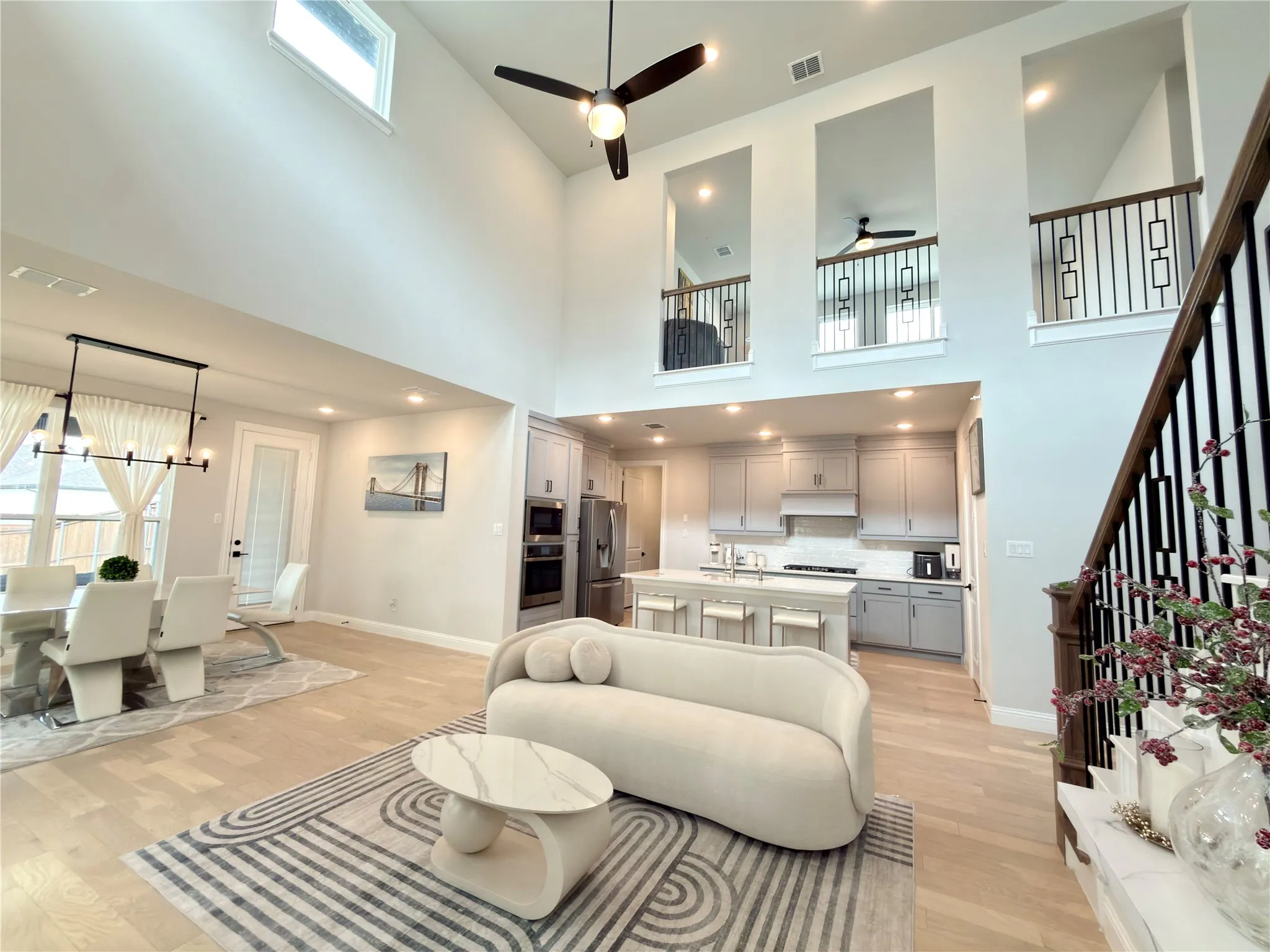 Open-concept living area featuring a two-story ceiling with high windows, light wood-finish flooring, and recessed lighting