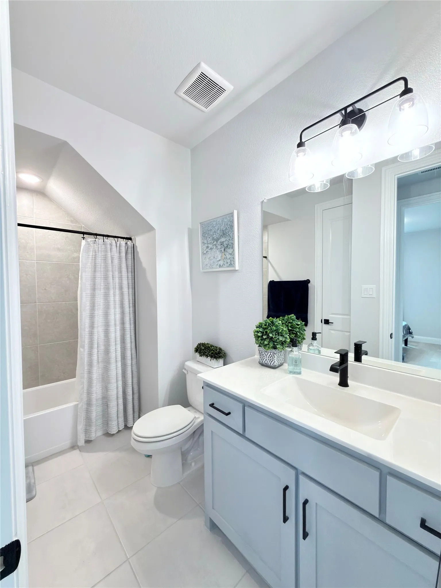 Modern bathroom featuring a single vanity with light blue cabinetry and matte black hardware, a white countertop with an integrated sink, a rectangular mirror, and a three-light vanity fixture
