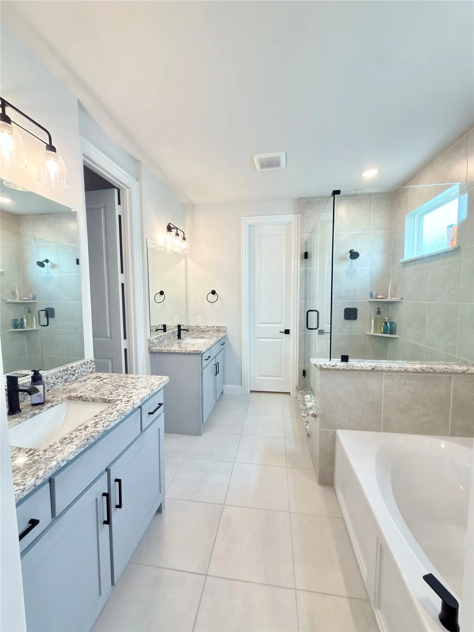 Spacious bathroom featuring a built-in soaking tub, a walk-in shower with clear glass enclosure, and dual vanity areas with light-colored cabinetry and stone countertops