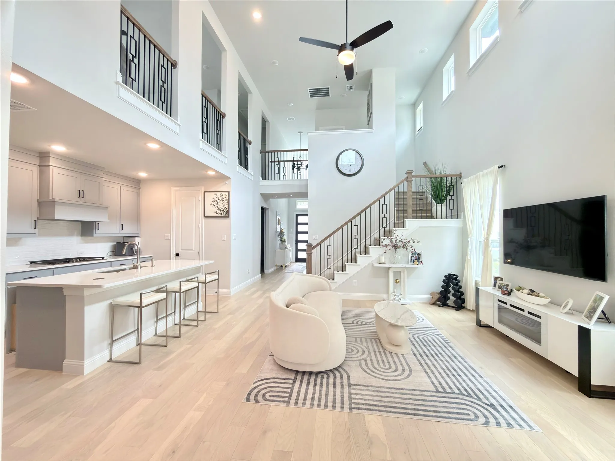 Open-concept living space featuring high ceilings, light wood-finish flooring, and a contemporary kitchen with light gray cabinetry and a white countertop island