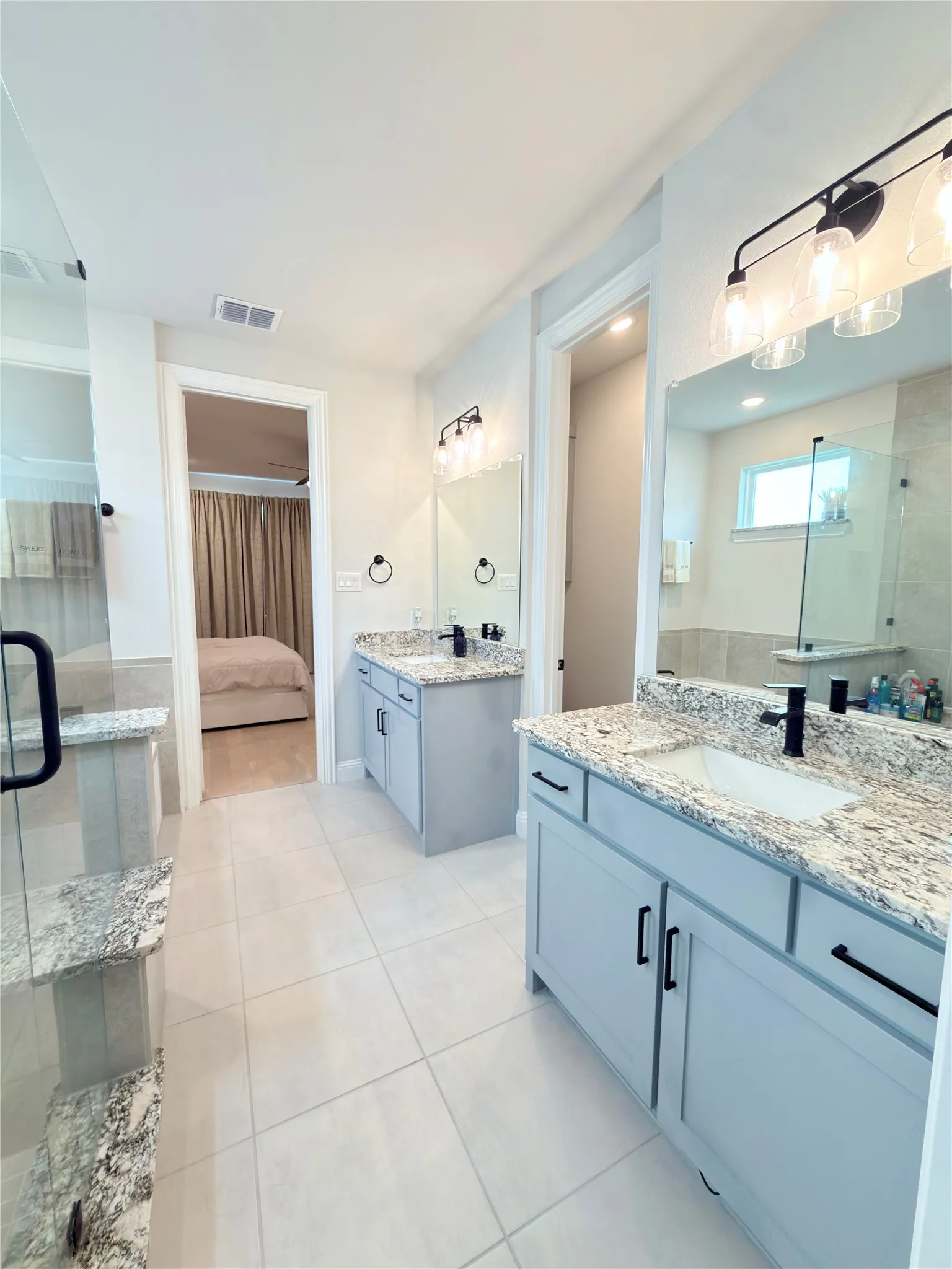 Dual vanity bathroom featuring light-colored cabinetry with black hardware, granite countertops, and under-mount sinks