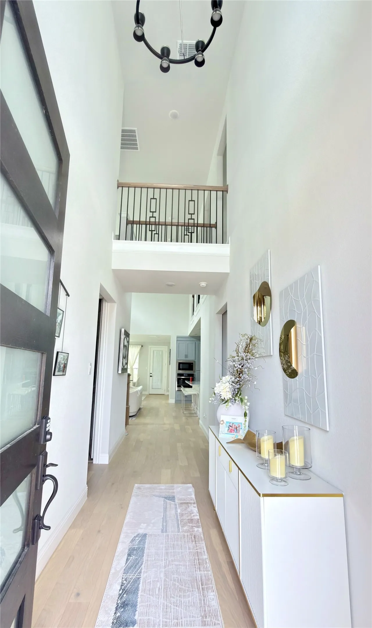 Two-story entryway with a black chandelier, light wood-finish flooring, and a second-story landing featuring a wood handrail and black metal spindles