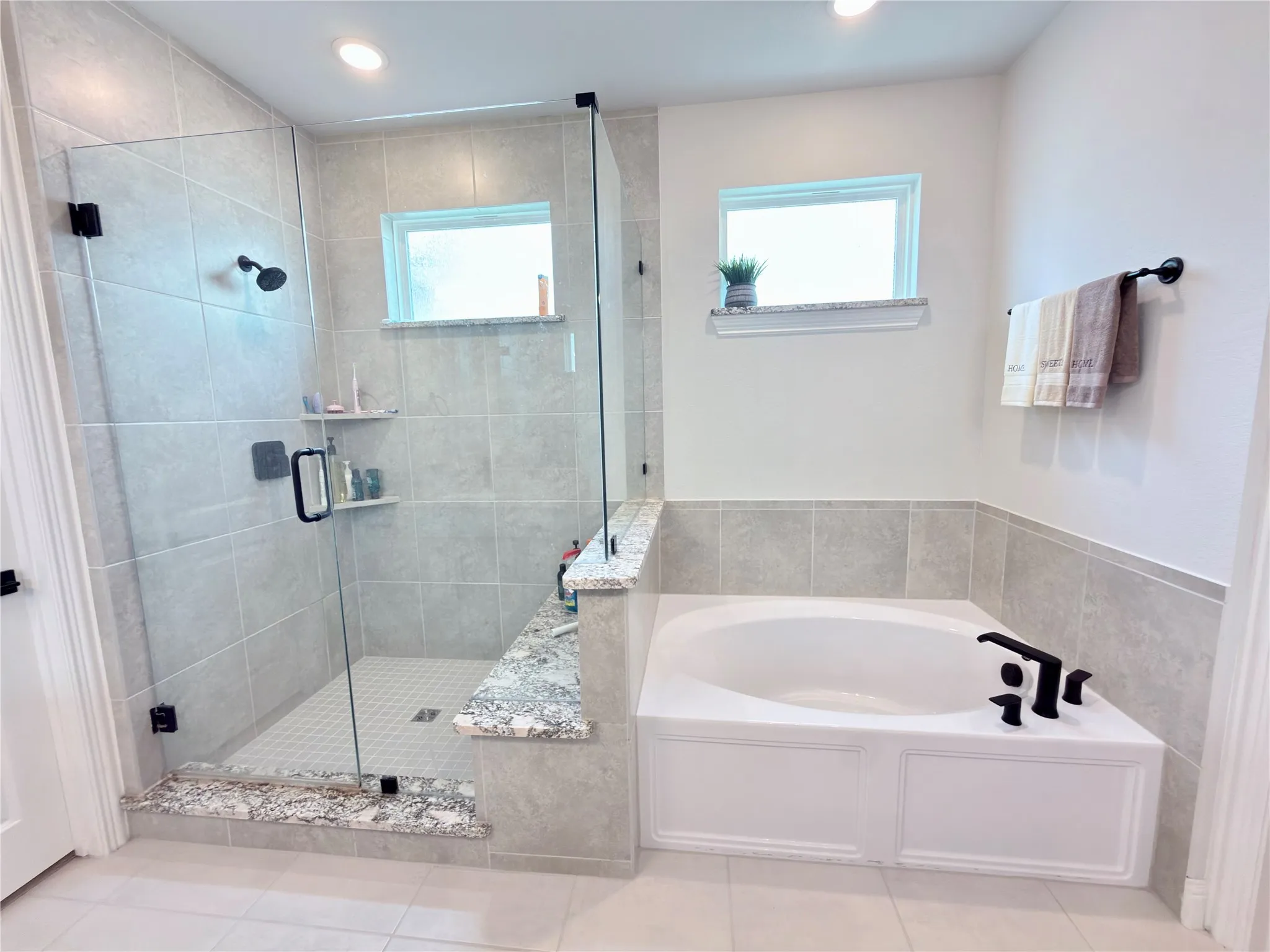 Walk-in shower with clear glass enclosure and black hardware, complemented by a built-in corner tub featuring black fixtures