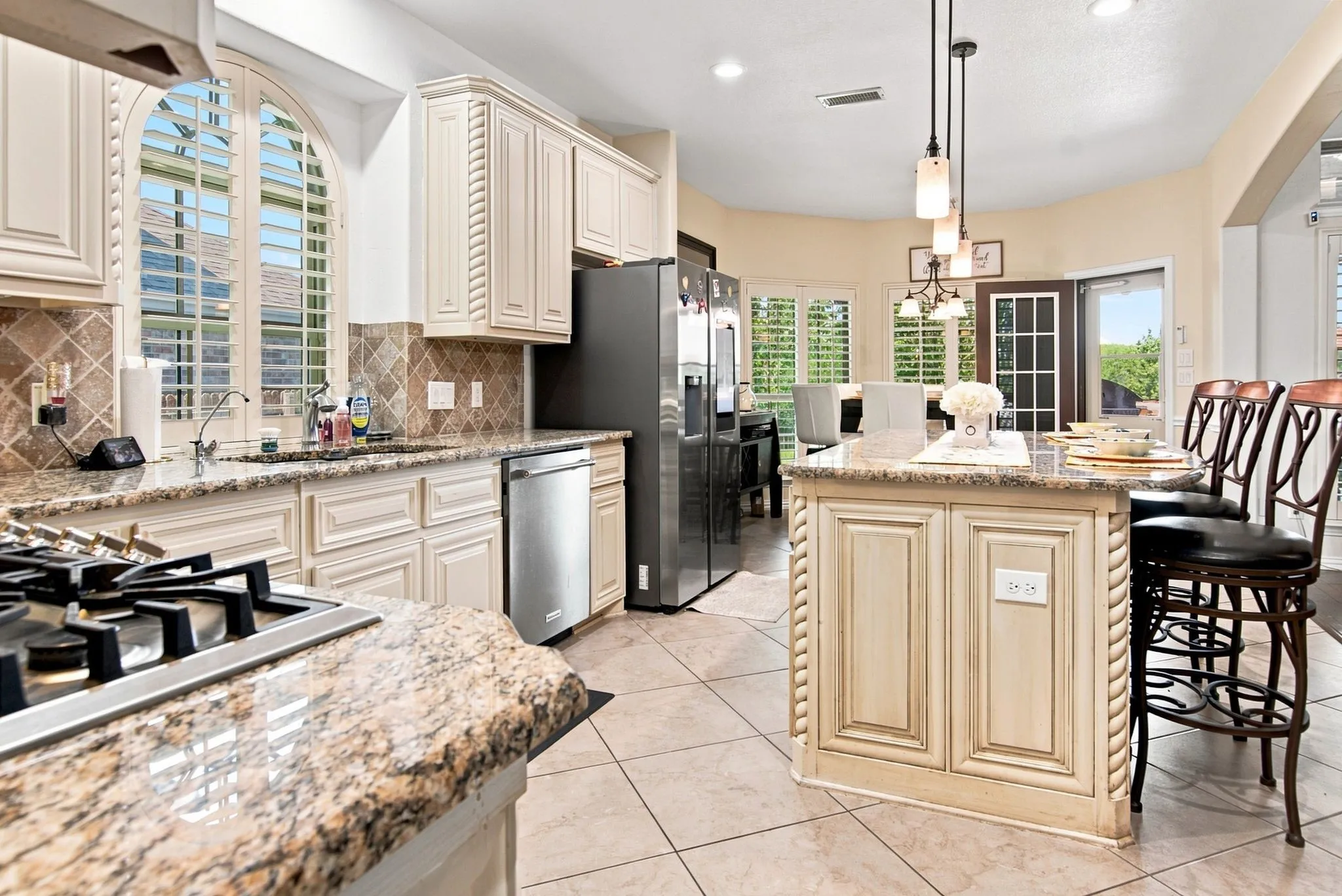 Kitchen featuring granite countertops, integrated cooktop, stainless steel dishwasher, and an arched window with louvered shutters