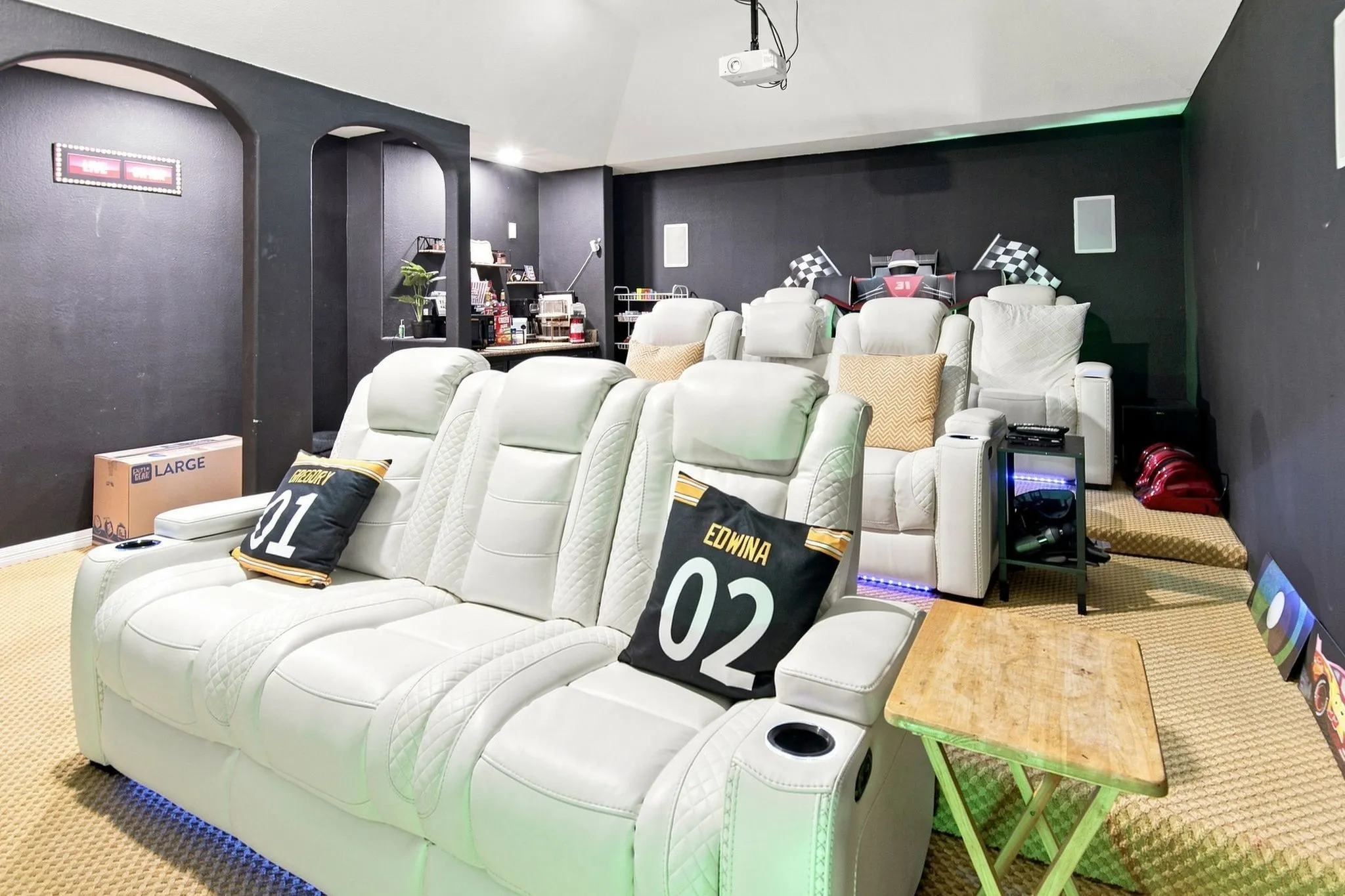 Dedicated media room featuring tiered seating, dark-painted walls, and a ceiling-mounted projector