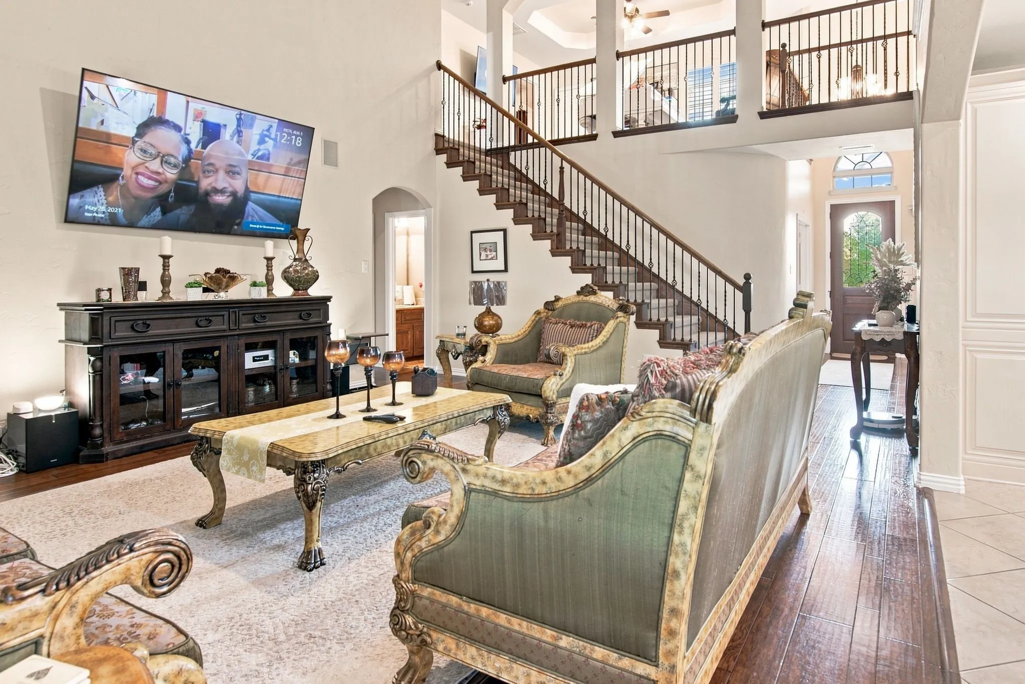 Two-story living area featuring wood-finish flooring, a grand staircase with dark wood railings, and a balcony overlook