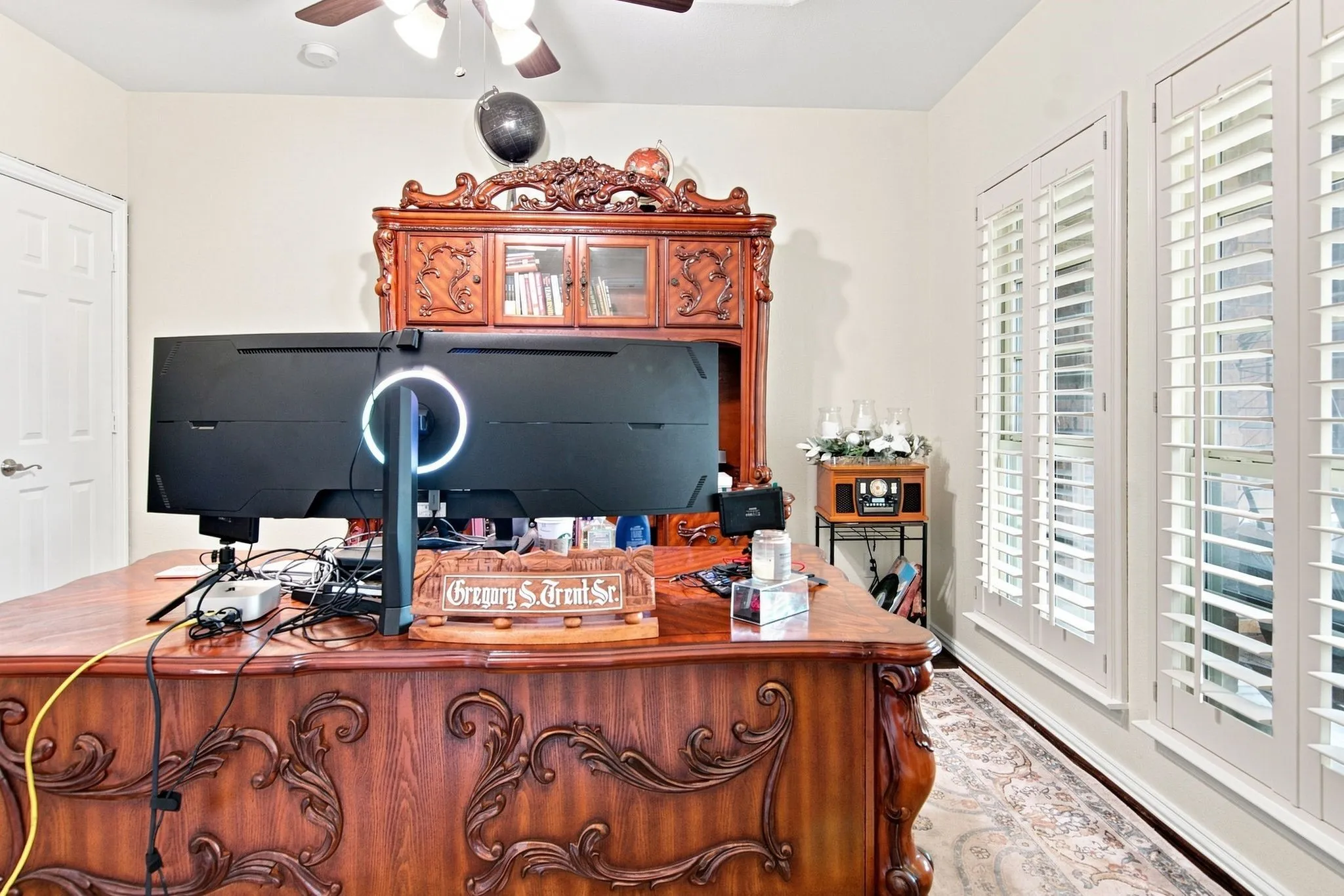 Custom window shutters complement the interior, featuring a ceiling fan, a paneled door, and neutral wall tones