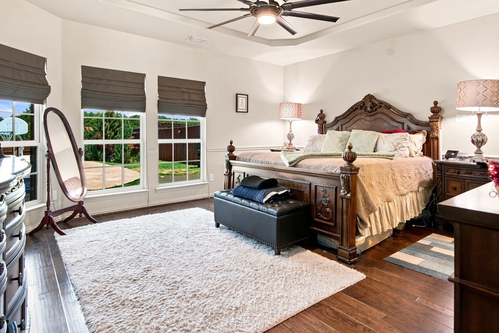 Spacious room featuring wood-finish flooring, tray ceiling with a ceiling fan, and multiple windows with privacy shades