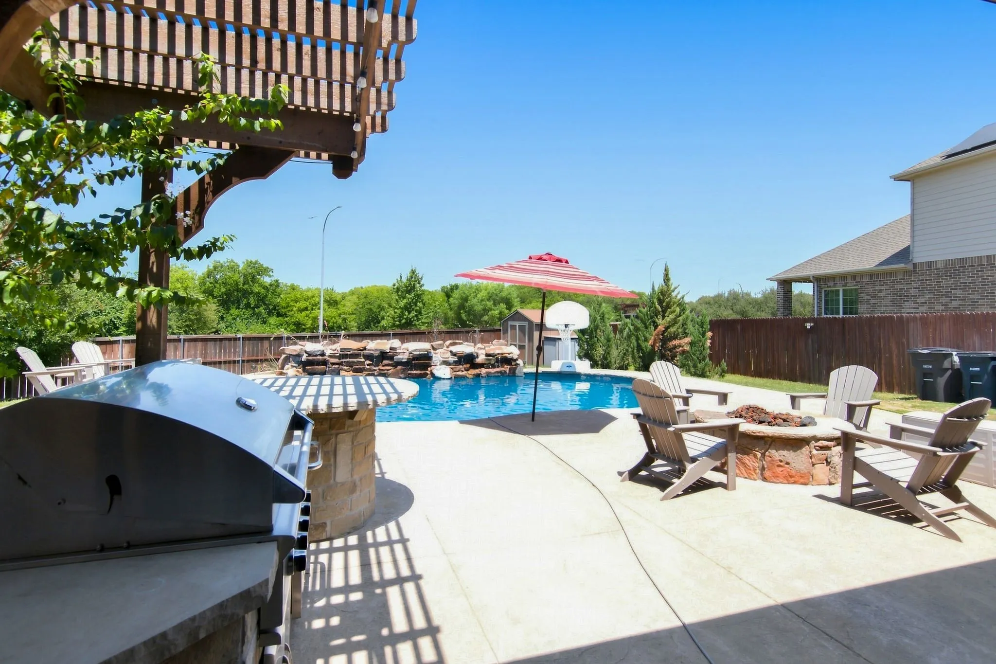 Outdoor living space featuring a built-in stone fire pit, concrete patio, and a swimming pool with a rock waterfall