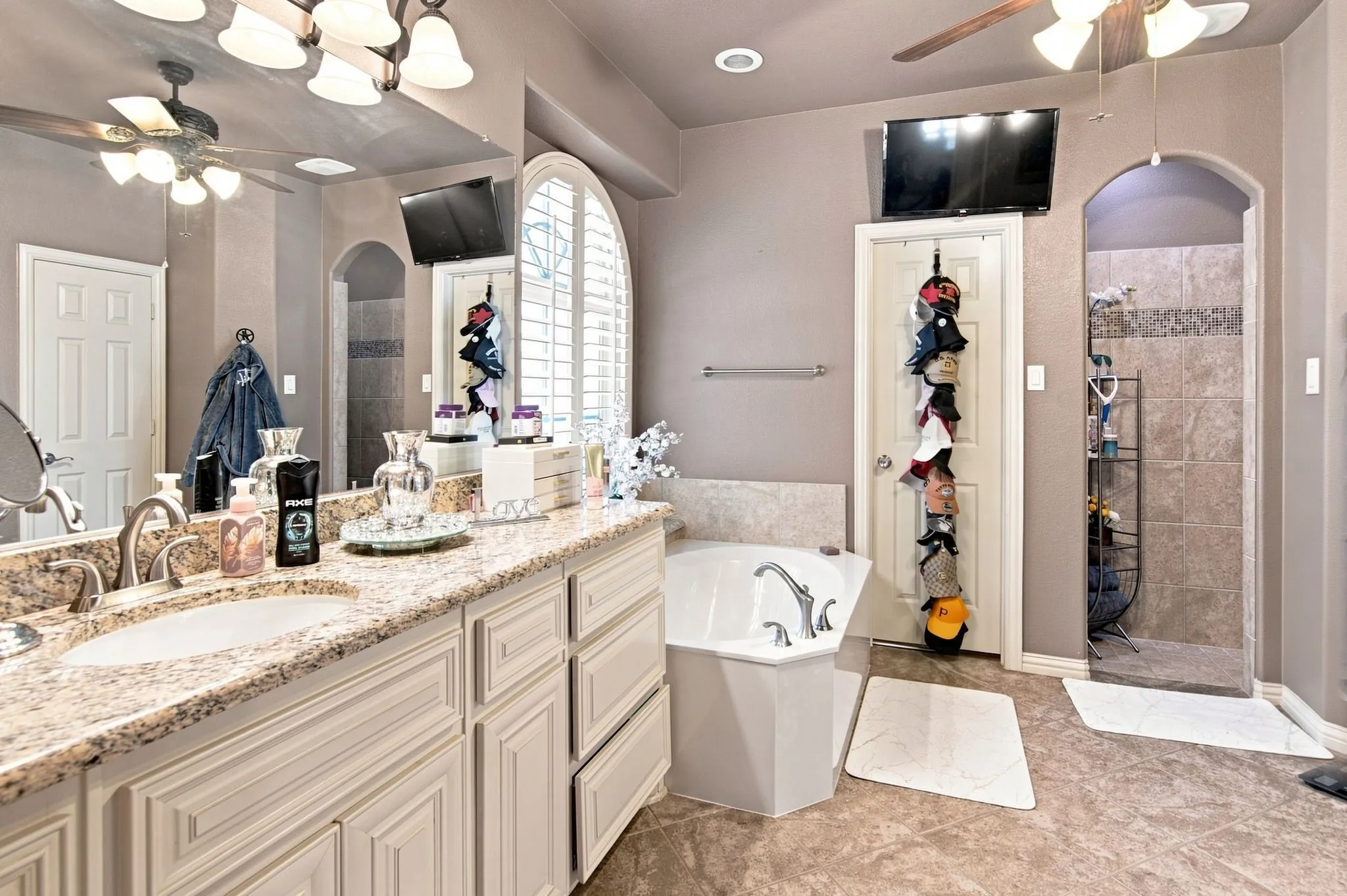 Spacious bathroom featuring a dual vanity with a light-toned granite countertop and white cabinetry, a separate corner soaking tub, and a shower with tiled walls