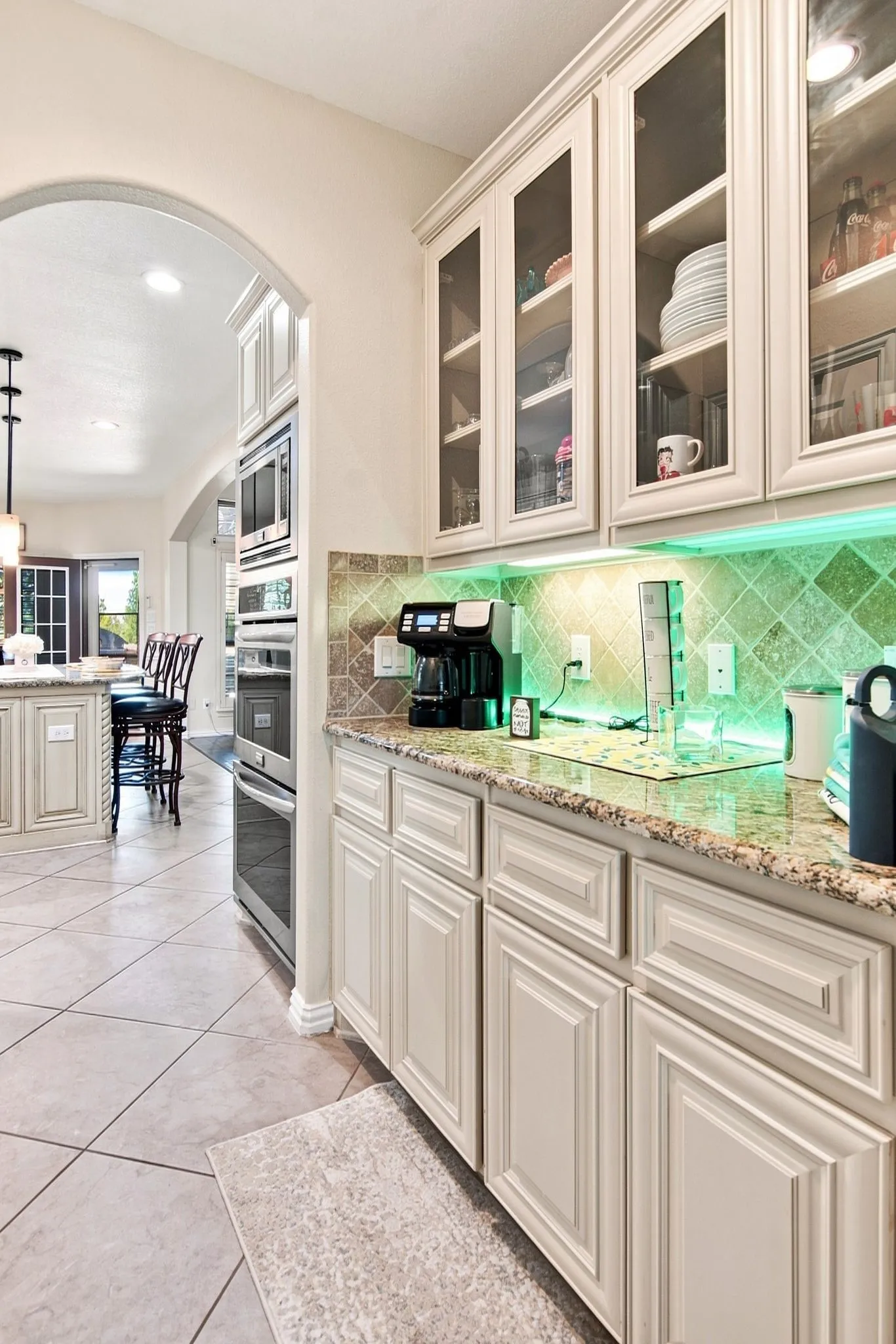 Kitchen featuring cream-colored cabinetry, glass-front upper cabinets, light-toned granite countertops, and a tile backsplash