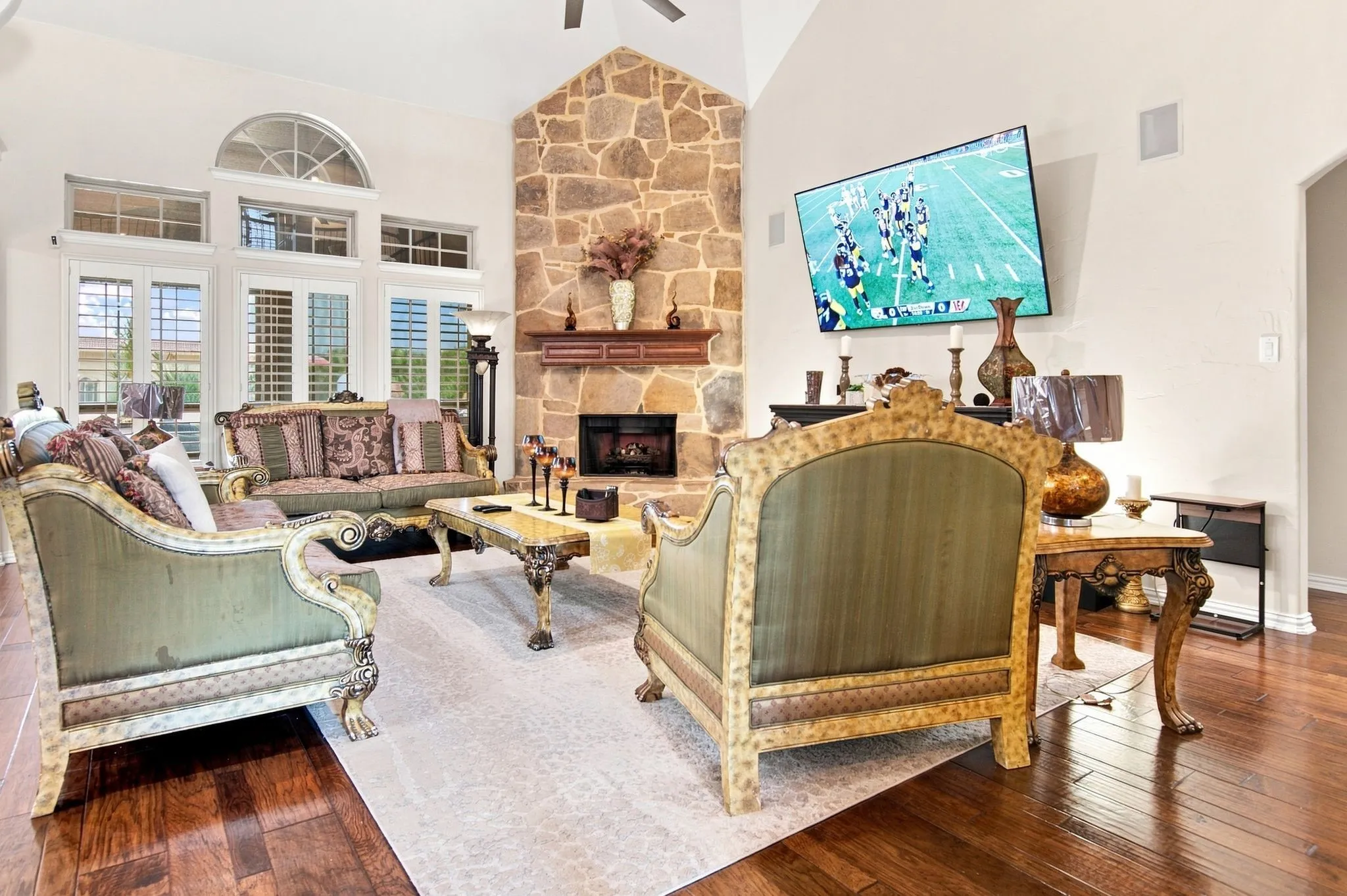 Spacious living area featuring a vaulted ceiling, a stone-clad fireplace with a wood mantel, and expansive windows with plantation shutters