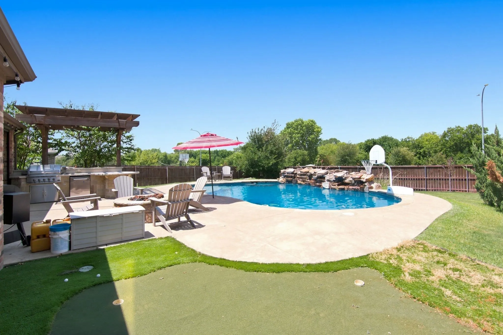 Resort-style backyard oasis featuring a free-form saltwater pool with integrated spa, expansive concrete decking, mature landscaping, and covered lounge areas with built-in outdoor kitchen and dining spaces