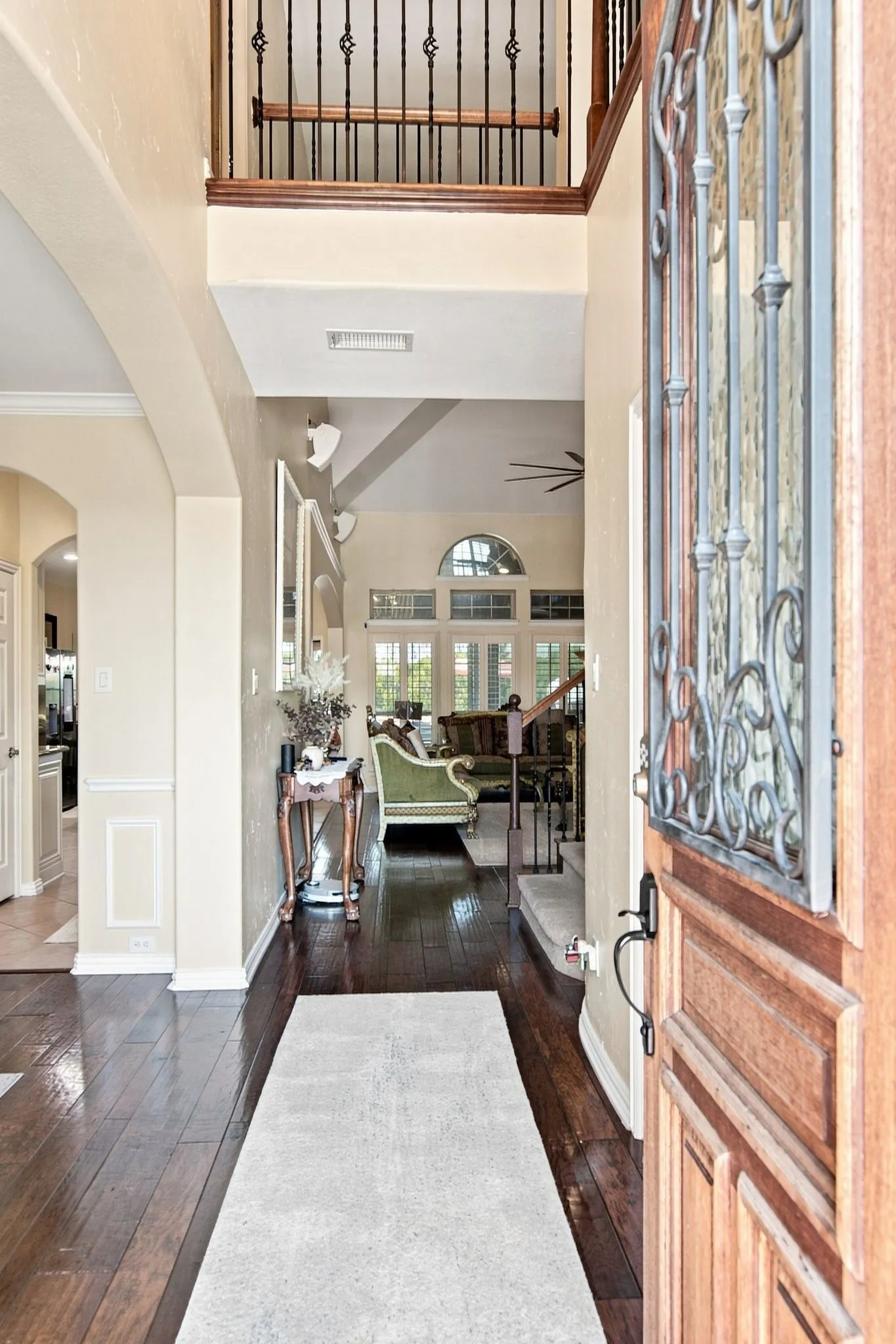 Grand entryway featuring rich wood-finish flooring, a decorative iron and wood staircase, and an arched doorframe