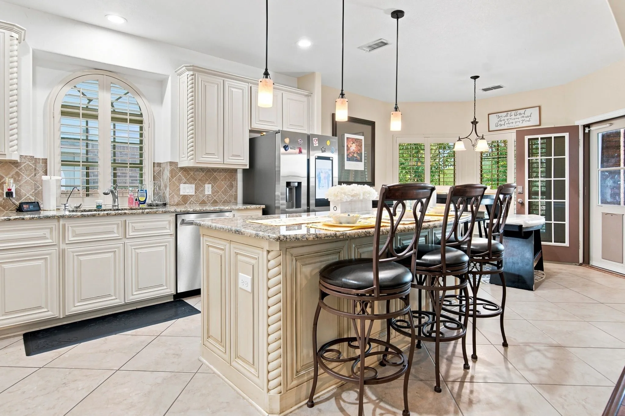 Chef's kitchen featuring cream-painted cabinetry with decorative molding, stainless steel appliances, light-filled breakfast bar with seating for four, pendant lighting, and tile flooring