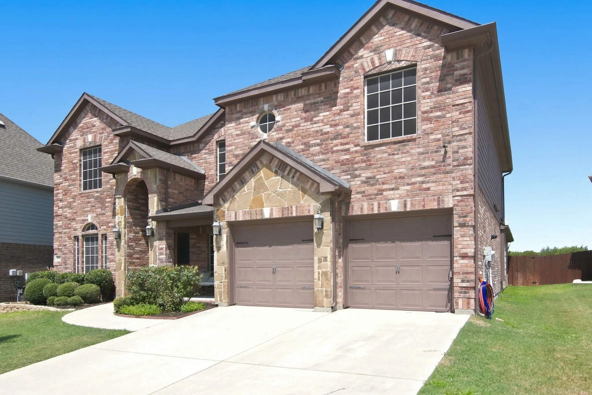 Two-story brick and stone veneer exterior featuring a prominent arched entry, two-car garage with individual doors, and a concrete driveway