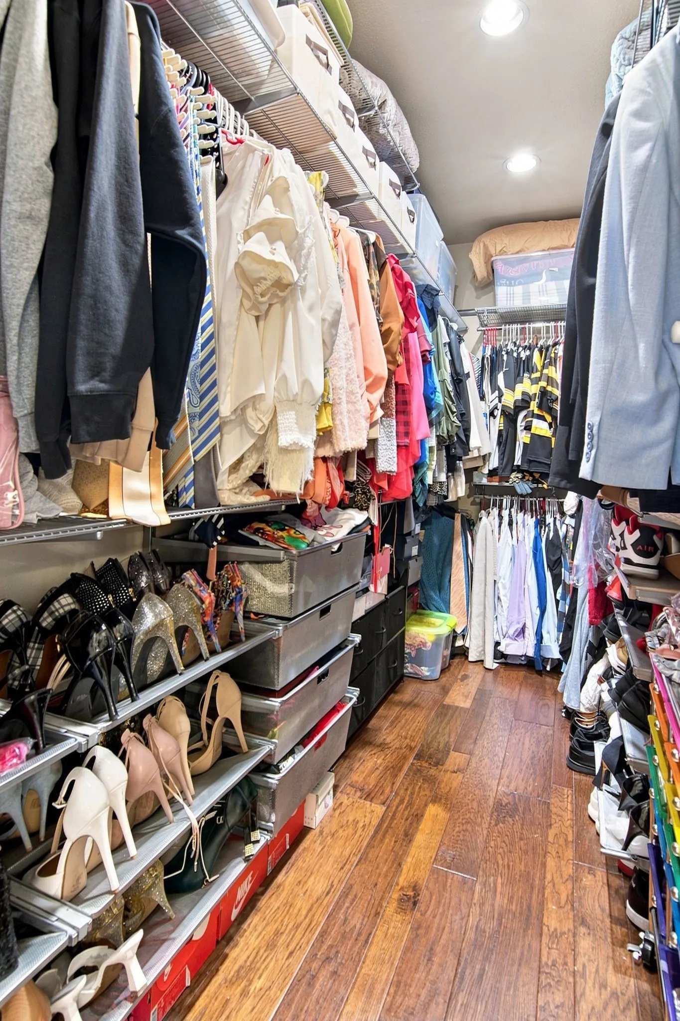 Custom closet featuring wood-finish flooring, recessed lighting, integrated shelving, and multiple hanging rods for ample storage