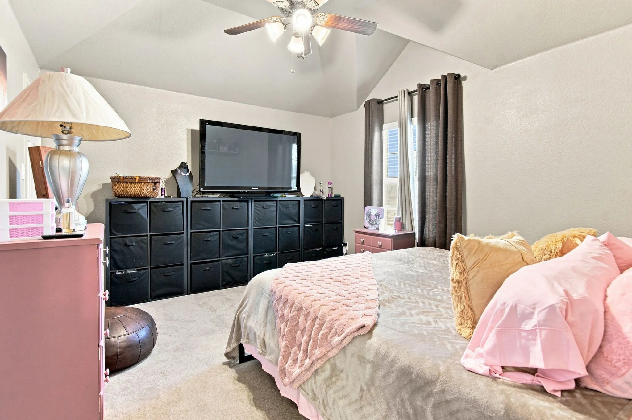 Carpeted room featuring a vaulted ceiling with a ceiling fan, light-colored walls, and natural light from a window with vertical blinds