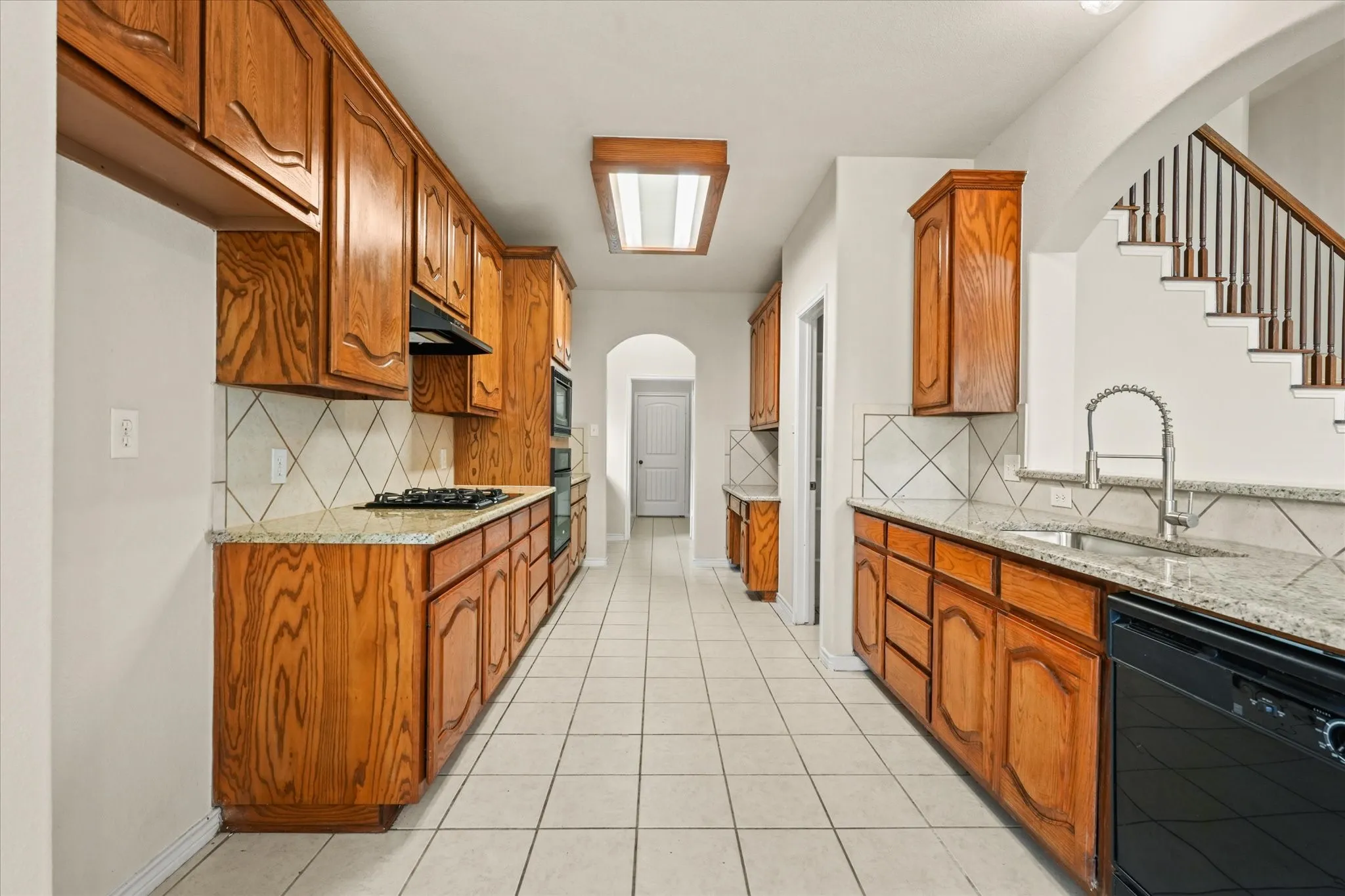 Kitchen with sink, black appliances, light stone countertops, and backsplash