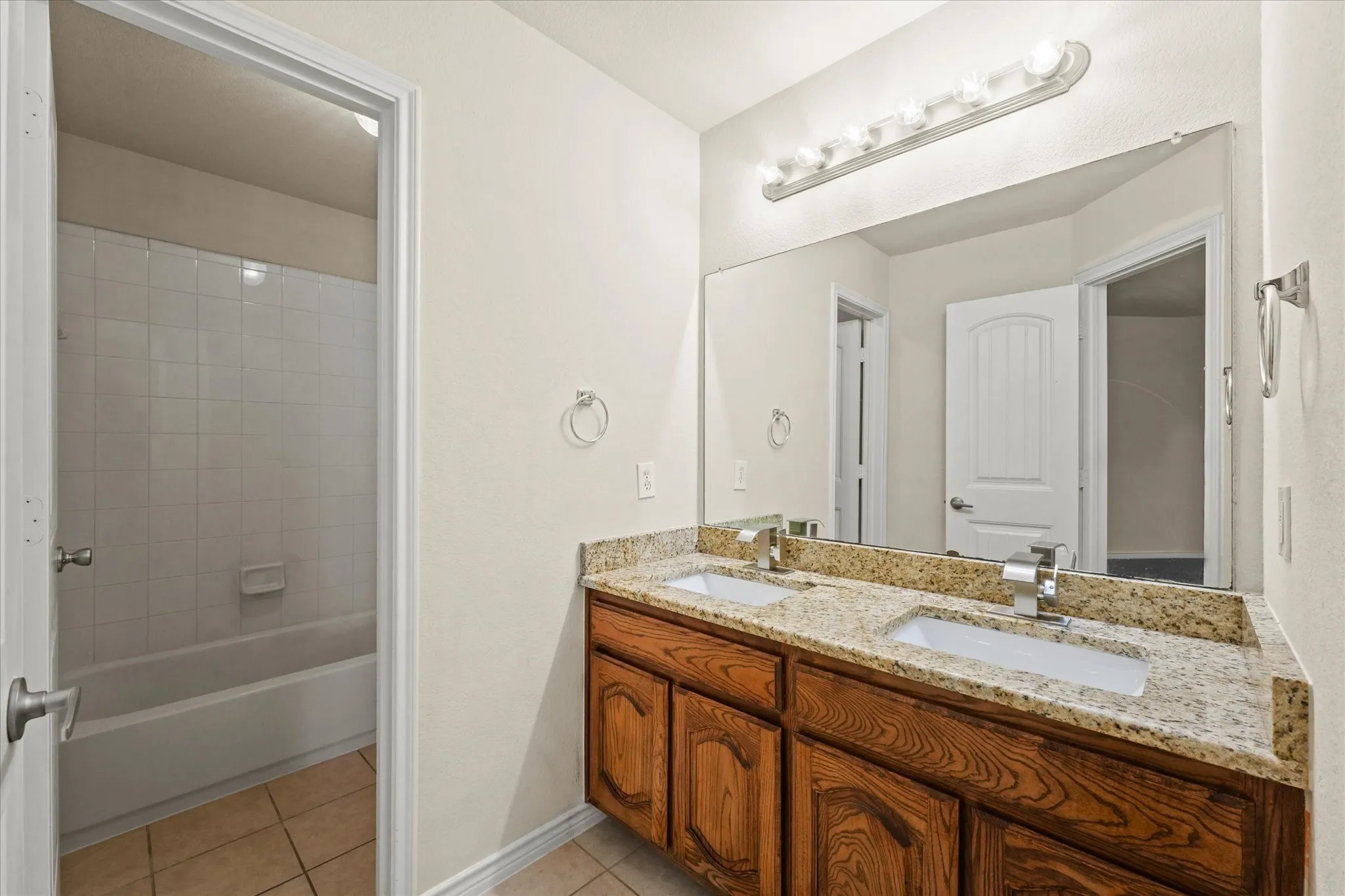Bathroom featuring dual bowl vanity, tiled shower / bath combo, and tile floors
