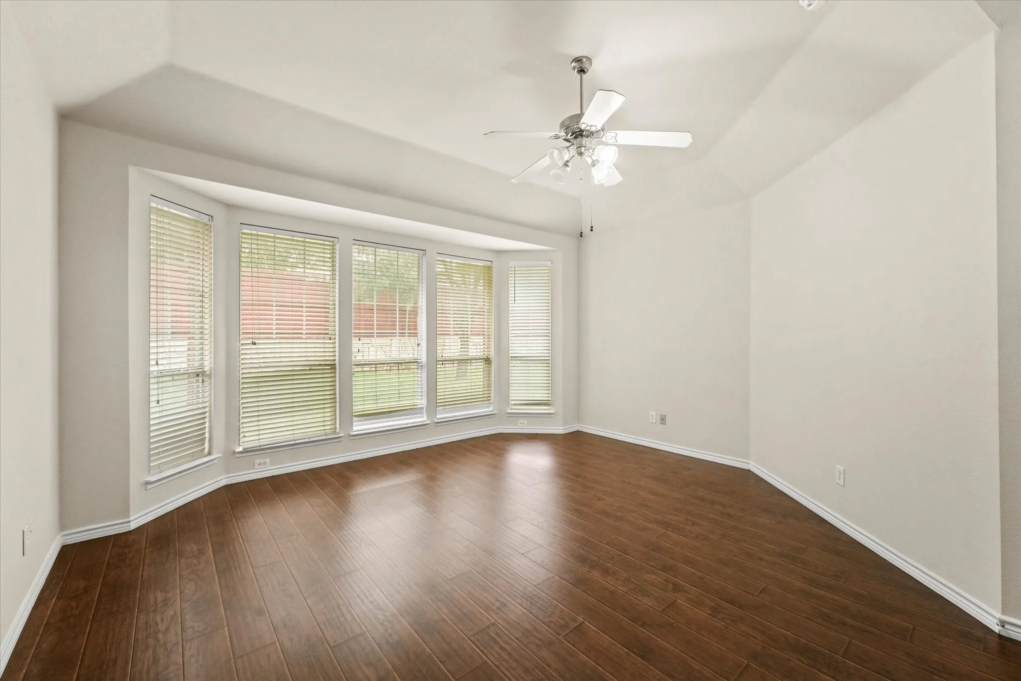 Empty room with dark hardwood / wood-style floors, ceiling fan, and a tray ceiling
