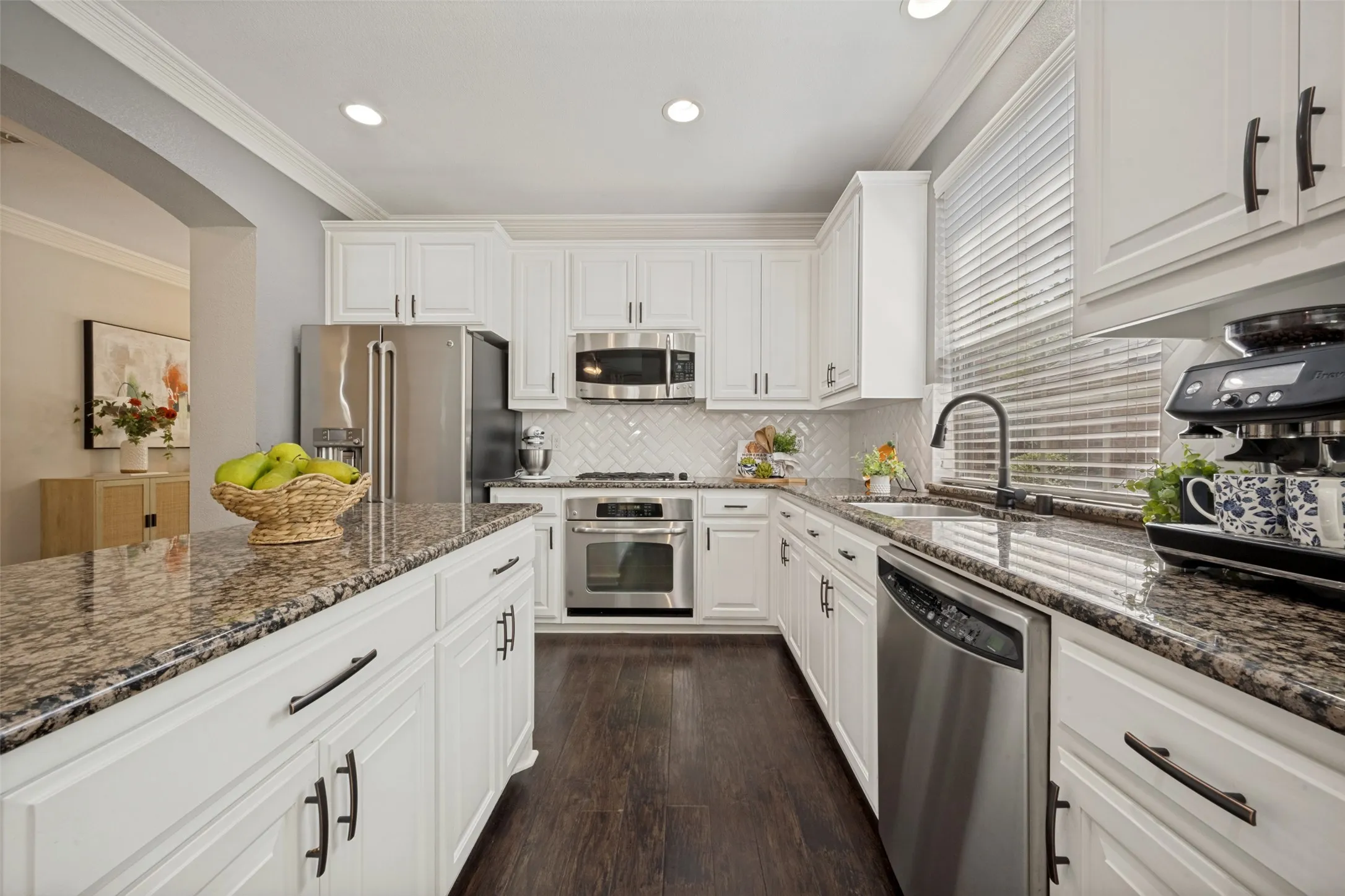 The heart of the home, this beautifully updated kitchen seamlessly blends timeless design with modern functionality. Crisp white cabinetry is complemented by elegant granite countertops, a stylish designer  backsplash, and rich hardwood flooring that adds warmth and sophistication. Abundant cabinet and countertop space make meal preparation effortless, while the oversized peninsula offers the perfect gathering spot for casual dining, entertaining, or morning coffee. Designed for both everyday living and entertaining, this stunning kitchen is a perfect combination of beauty, comfort, and practicality.