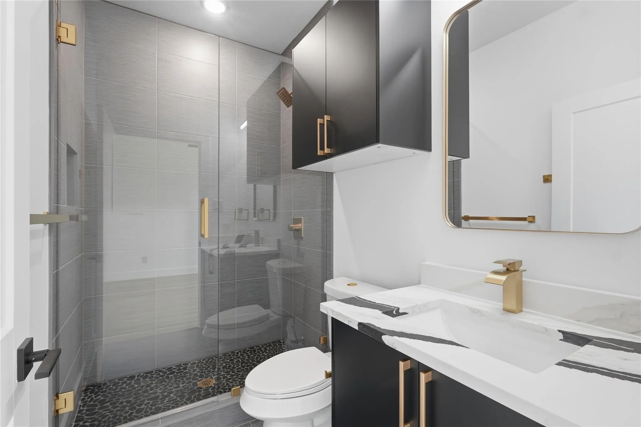 Contemporary bathroom featuring a frameless glass shower enclosure, dark pebble shower floor, and large format gray wall tiling