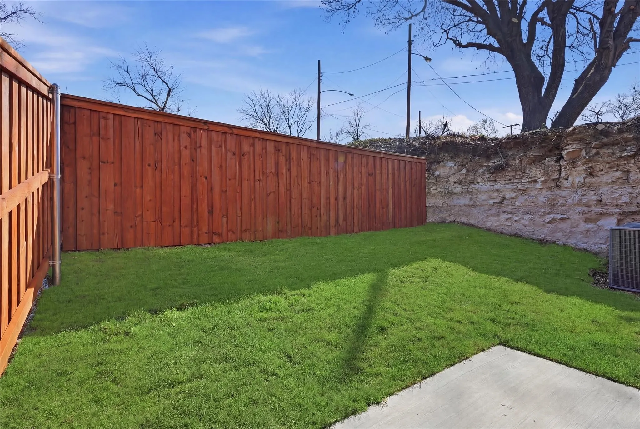 Expansive outdoor area featuring a newly installed wooden fence, lush green lawn, and a concrete patio